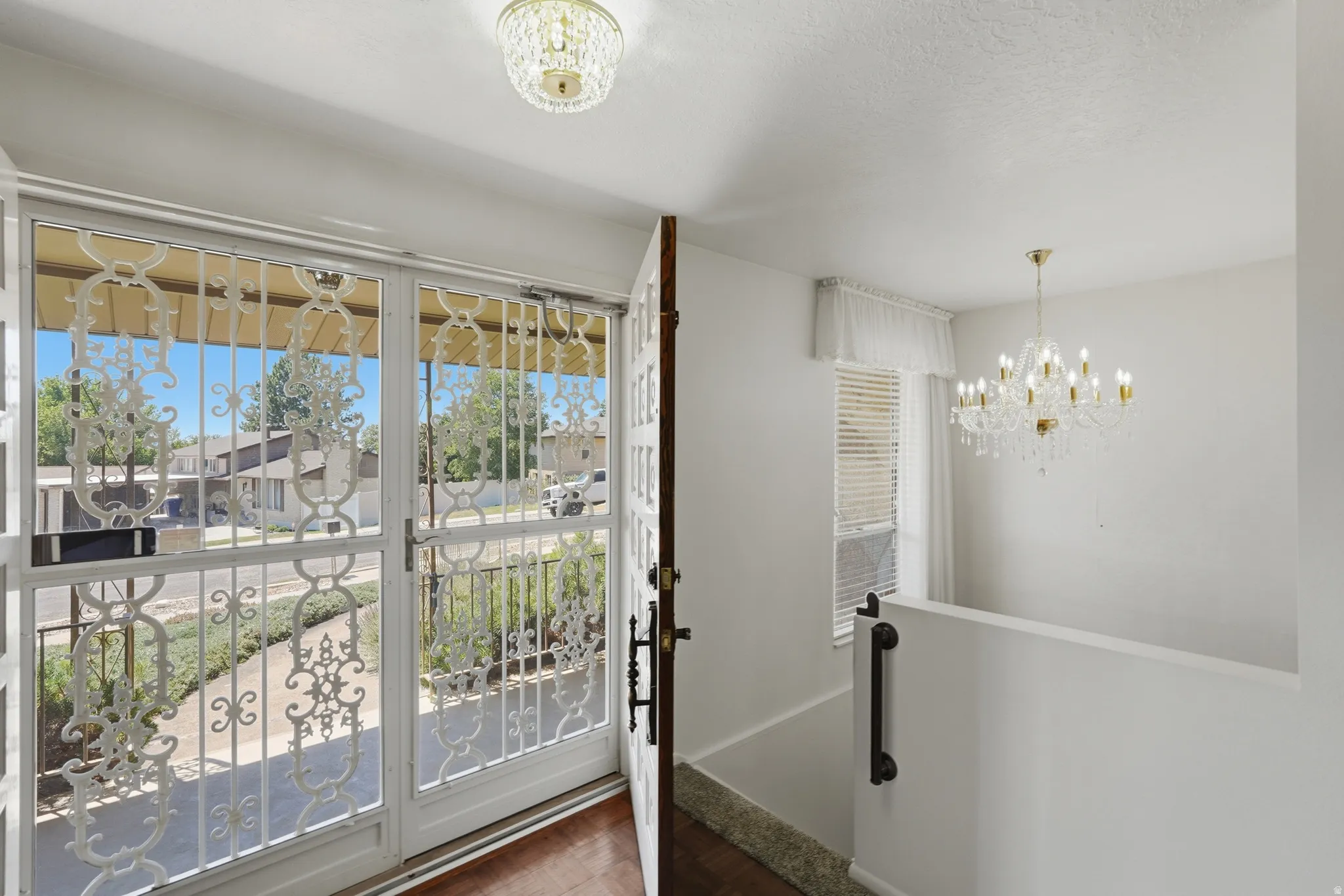 Entryway featuring security screen doors with decorative scrolling, a wood-finish floor, and a crystal chandelier