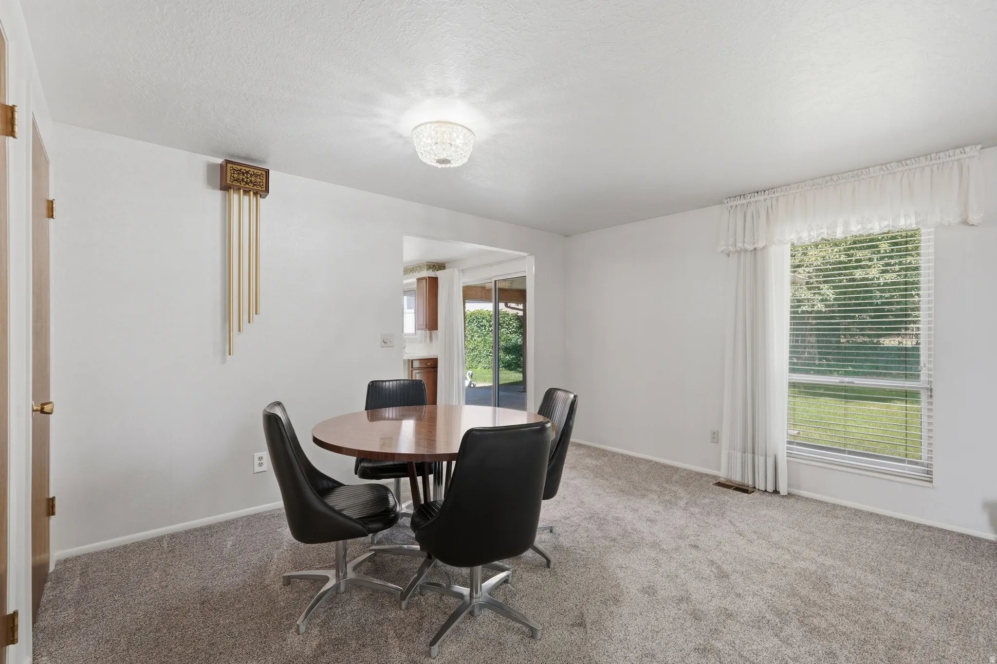 Carpeted room featuring a large window with blinds and white curtains, white walls, and a ceiling-mounted light fixture