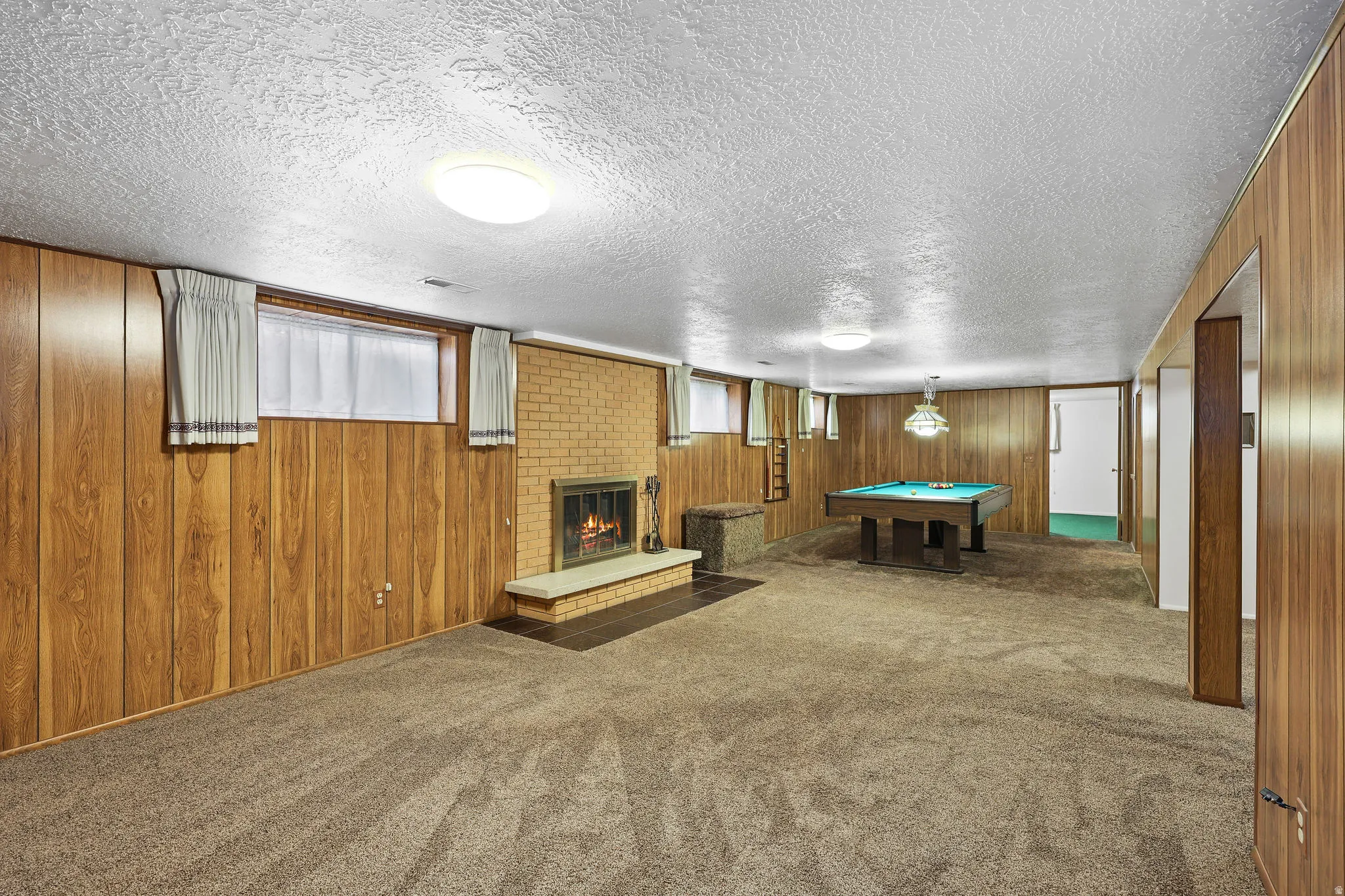 Game room featuring a brick fireplace, carpet, billiards table, a textured ceiling, and wooden walls