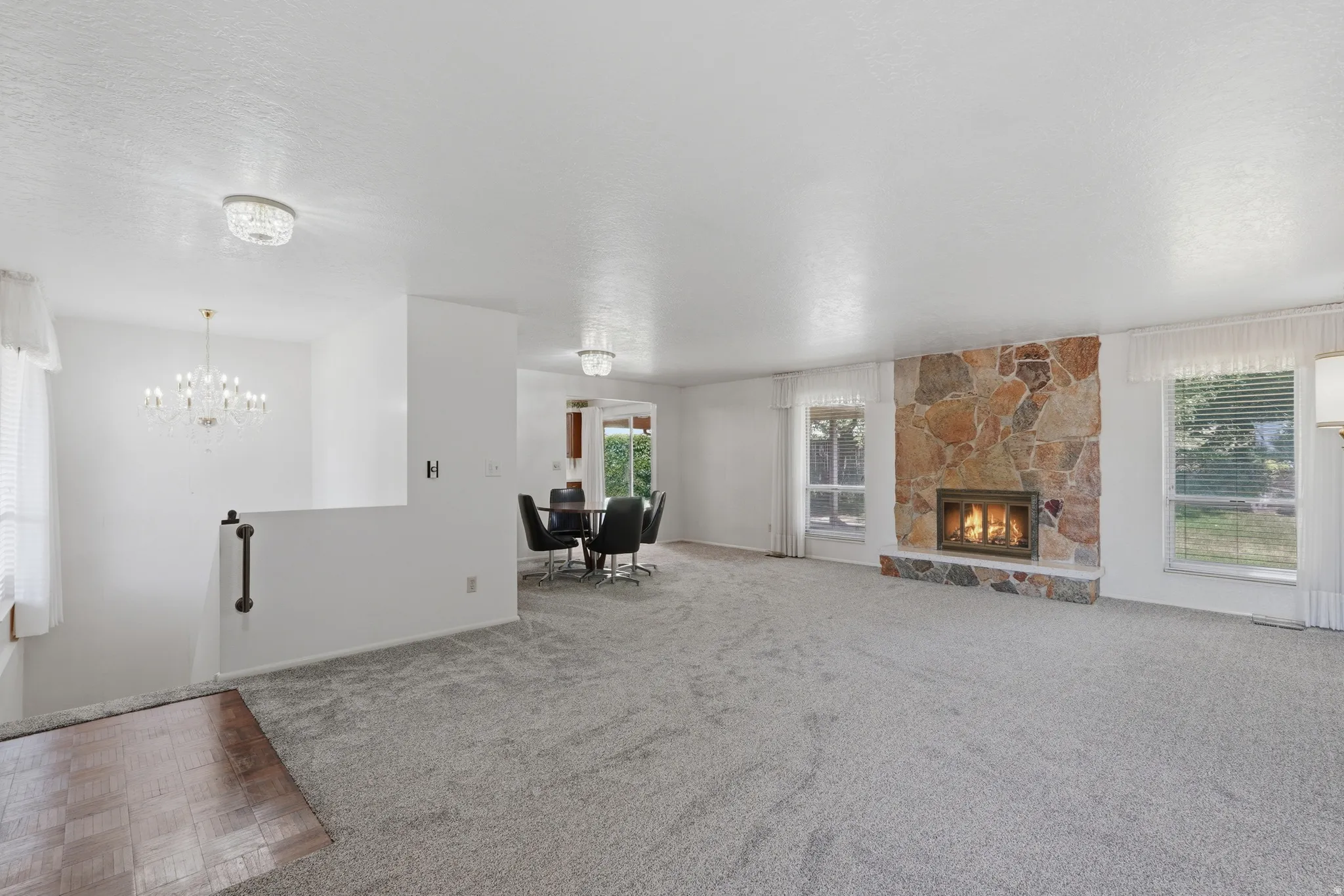 Spacious living area featuring a stone-faced fireplace with hearth, light gray carpeting, and multiple windows