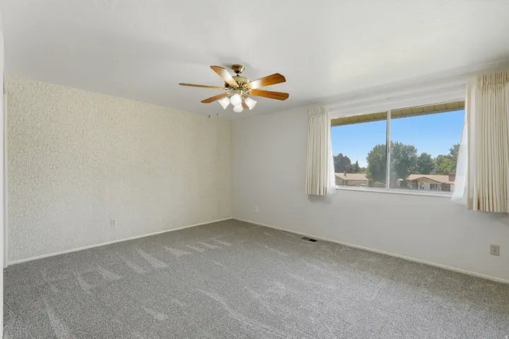 Spacious room featuring light gray carpet flooring and a ceiling fan with integrated lighting