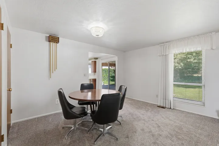Carpeted room featuring a large window with blinds and white curtains, white walls, and a ceiling-mounted light fixture