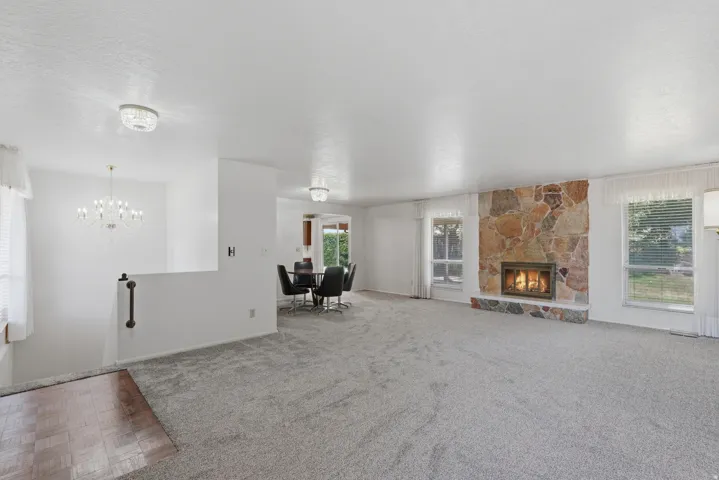 Spacious living area featuring a stone-faced fireplace with hearth, light gray carpeting, and multiple windows