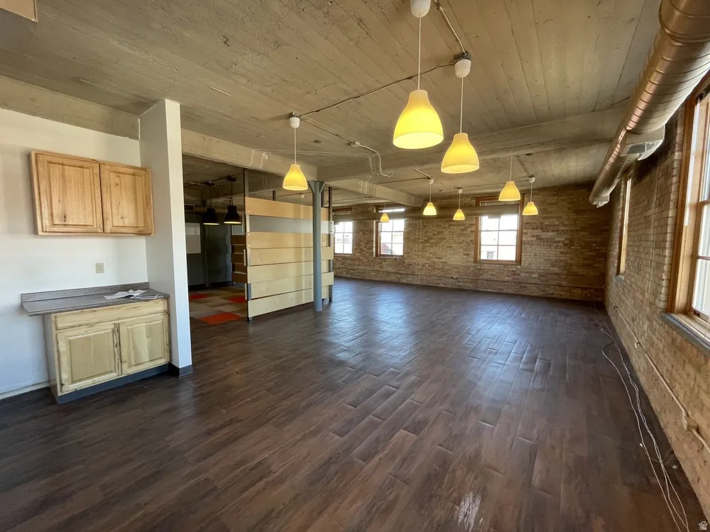 Unfurnished dining area featuring brick wall, dark wood-type flooring, and wooden ceiling