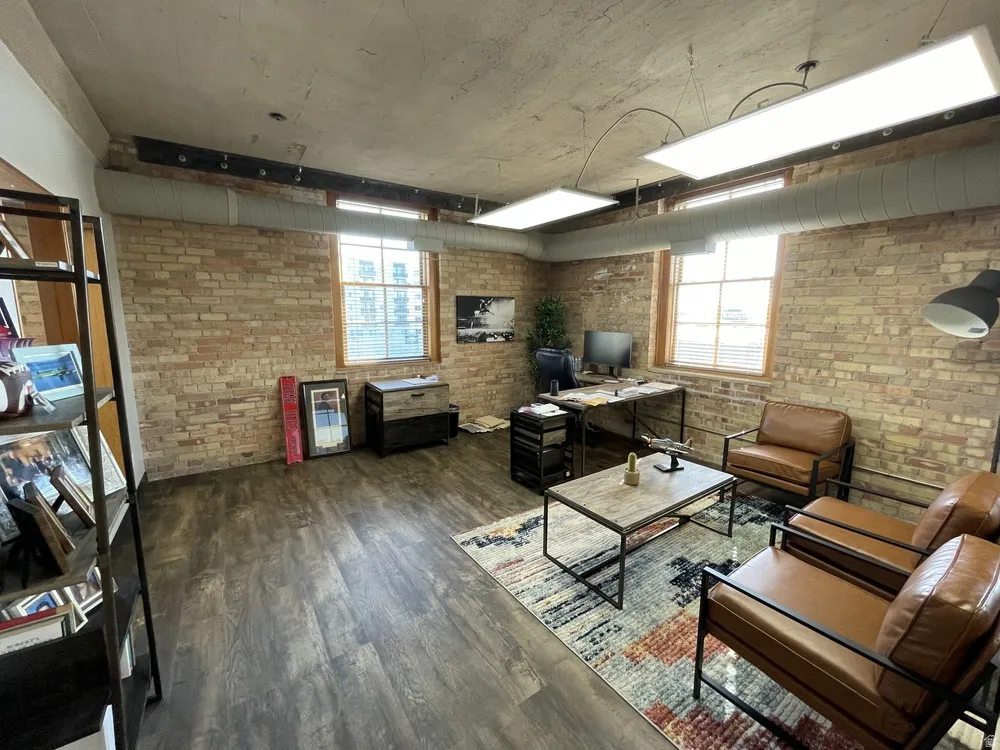 Living room featuring dark wood finished floors, plenty of natural light, brick wall, and a desk