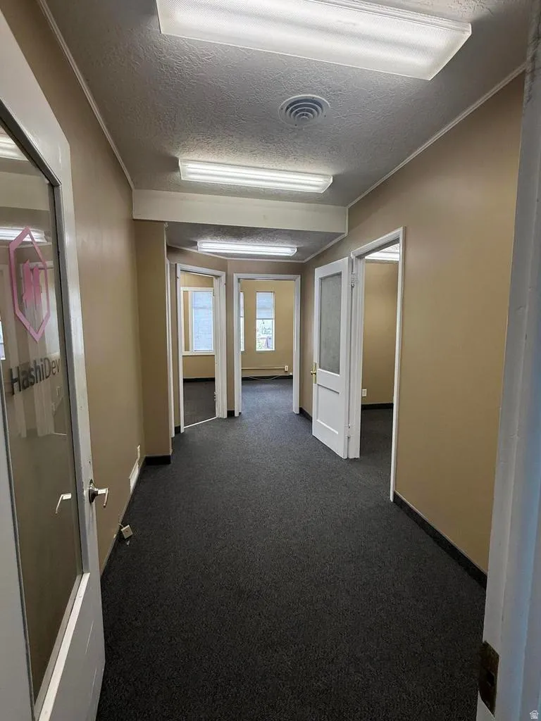 Hallway with a textured ceiling, dark carpet, and crown molding