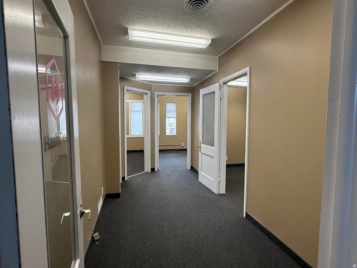 Hallway featuring a textured ceiling and dark colored carpet