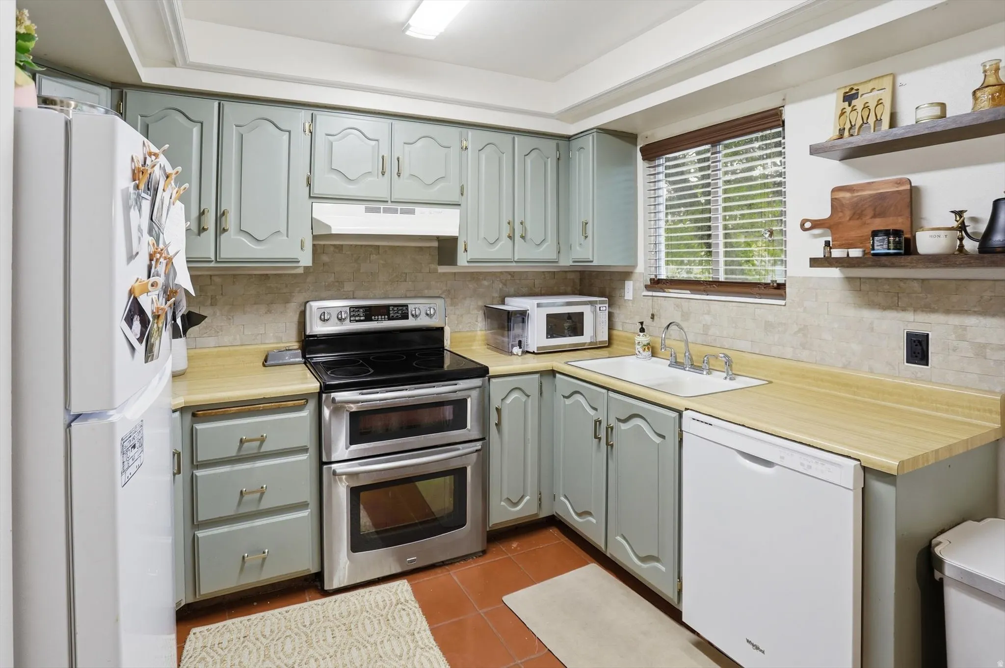 Kitchen with white appliances, light countertops, dark tile patterned flooring, open shelves, and backsplash