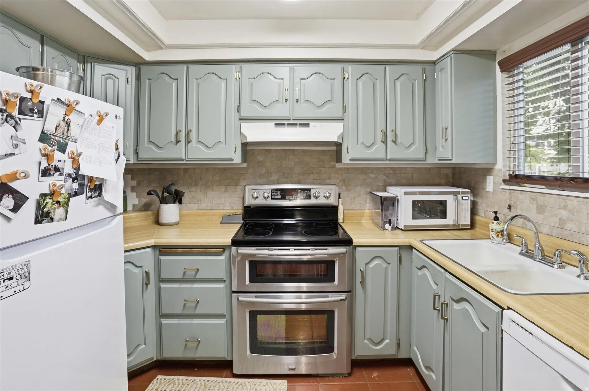 Kitchen featuring white appliances, light countertops, dark tile patterned floors, tasteful backsplash, and gray cabinetry