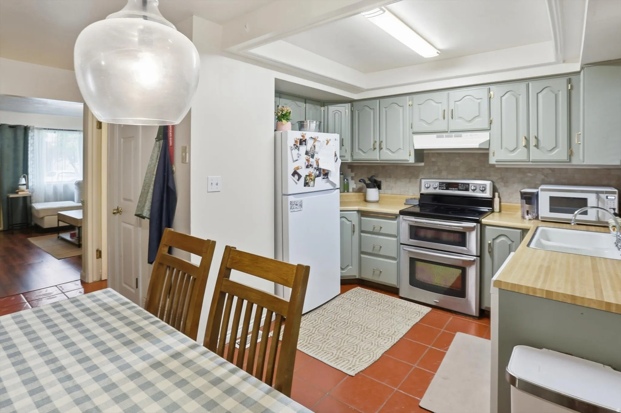 Kitchen featuring light countertops, white appliances, dark tile patterned flooring, and decorative backsplash