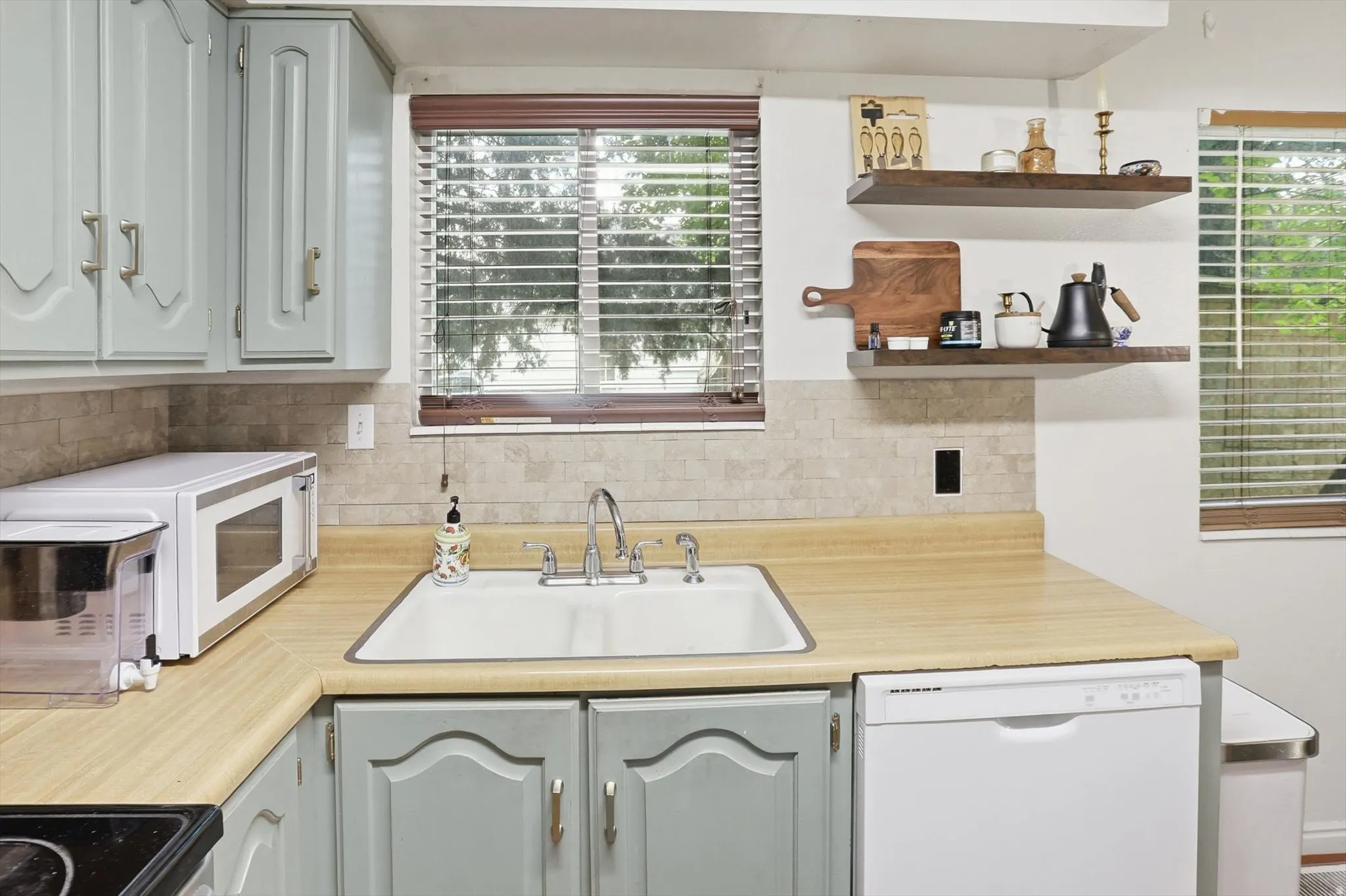 Kitchen featuring light countertops, white appliances, open shelves, and decorative backsplash