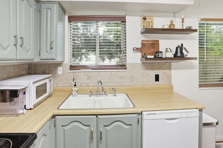 Kitchen featuring light countertops, white appliances, open shelves, and decorative backsplash