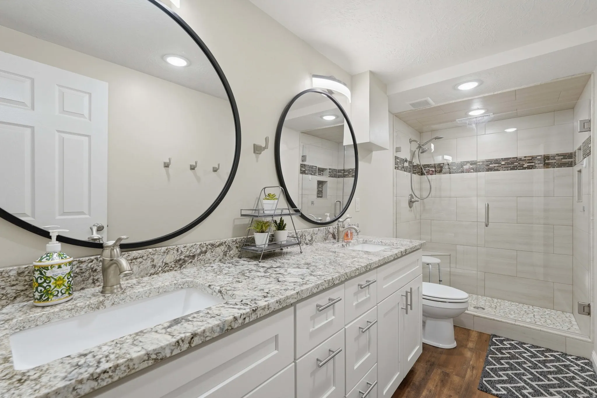 Bathroom with double vanity, a shower stall, dark wood-style flooring, and recessed lighting