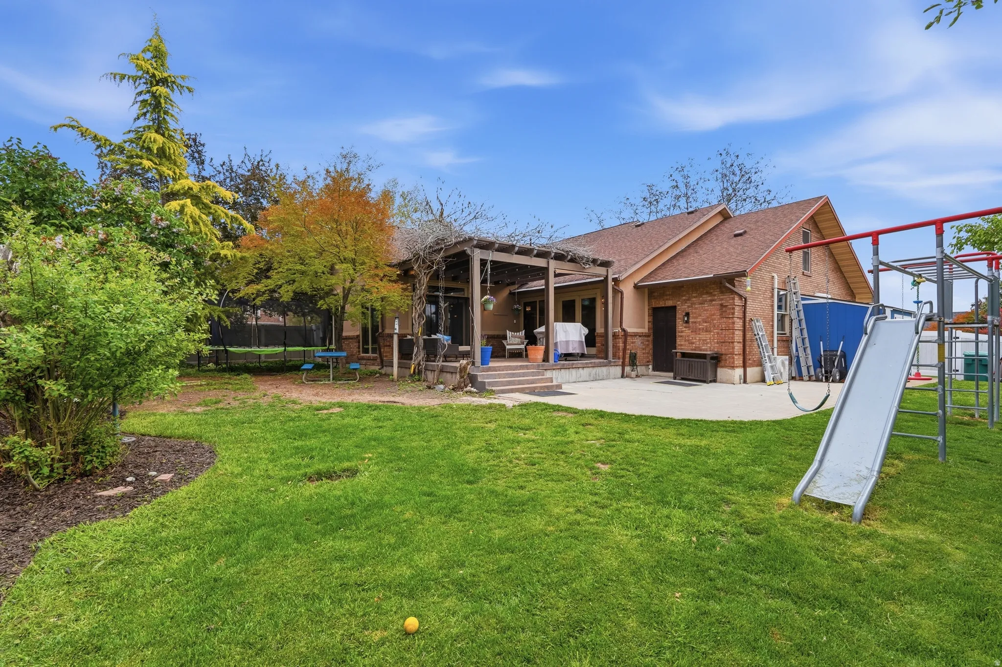 Rear view of house with a trampoline, a patio area, brick siding, and a shingled roof