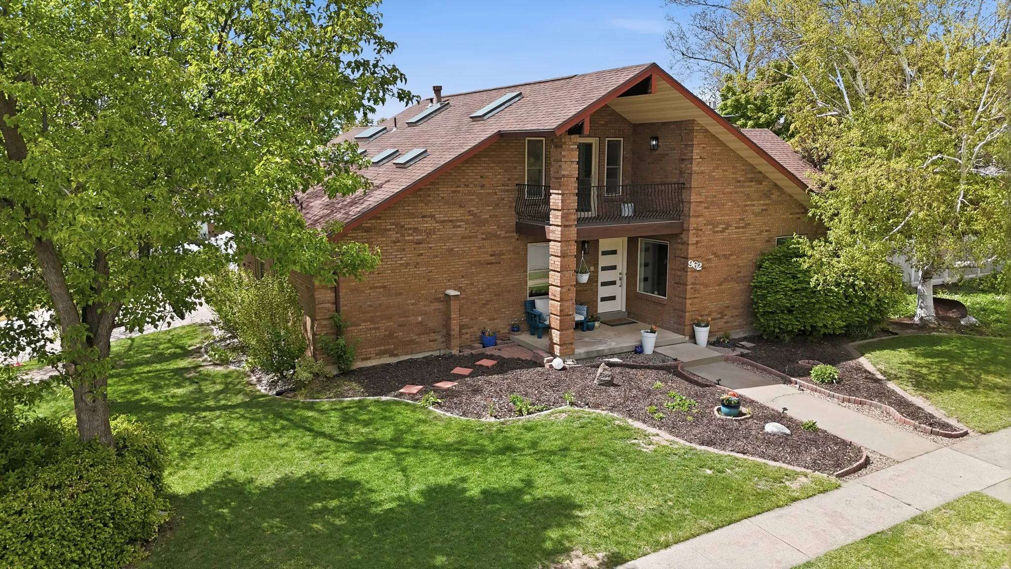 View of front of house featuring a front lawn, a balcony, roof with shingles, and brick siding