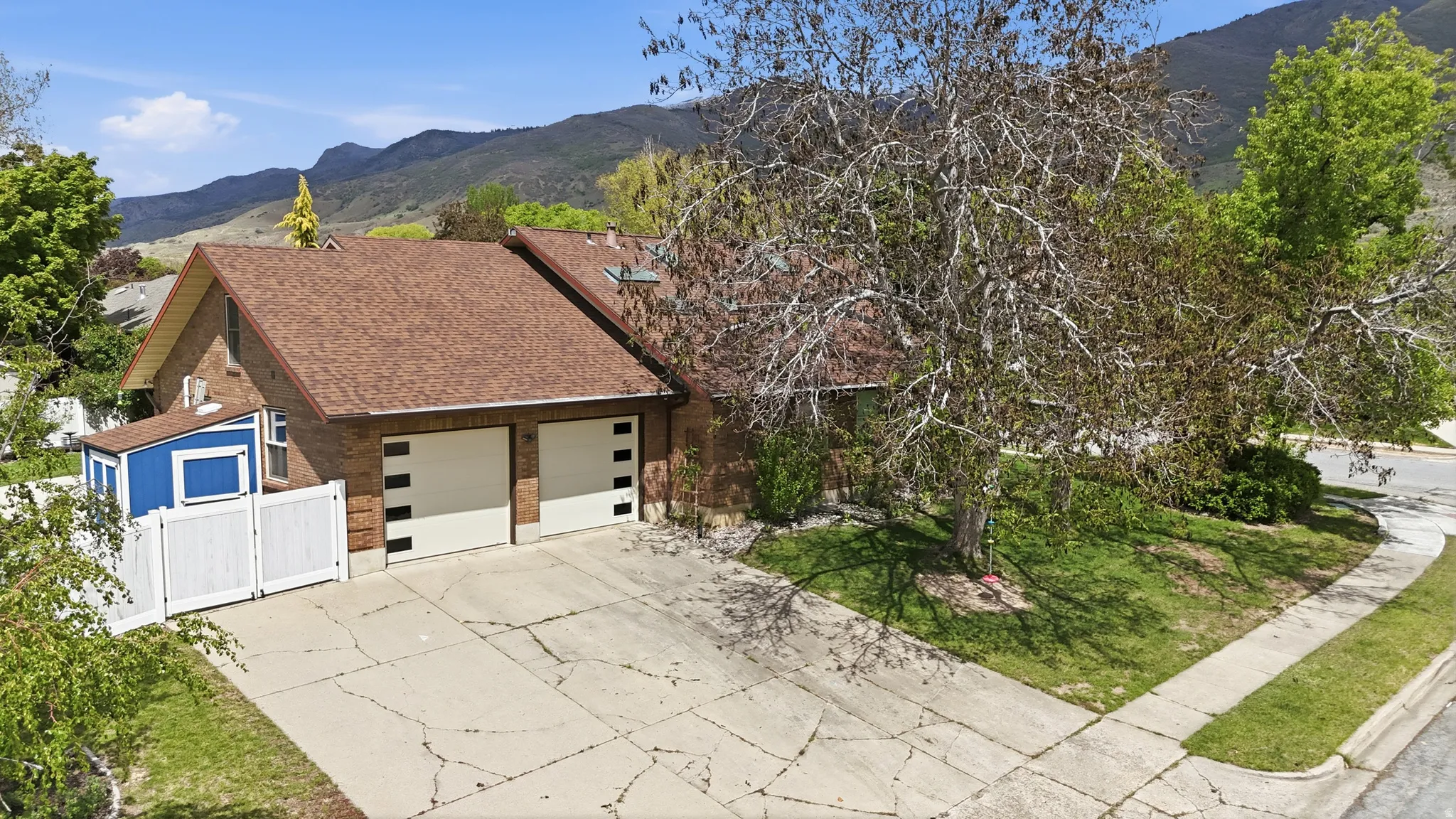 View of front facade with a mountain view, brick siding, a shingled roof, concrete driveway, and a gate