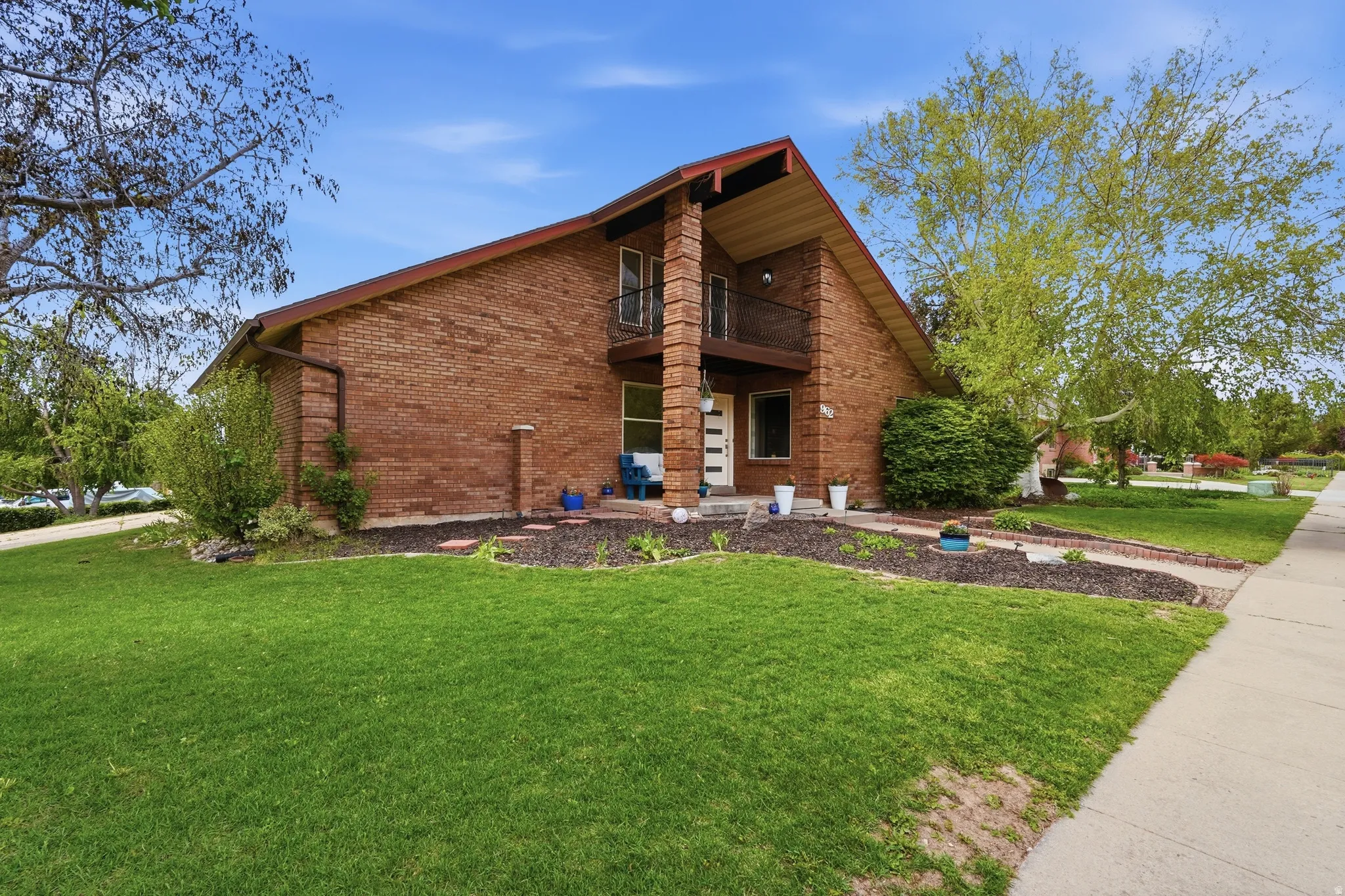 View of front facade with a balcony, a front yard, brick siding, and a patio area