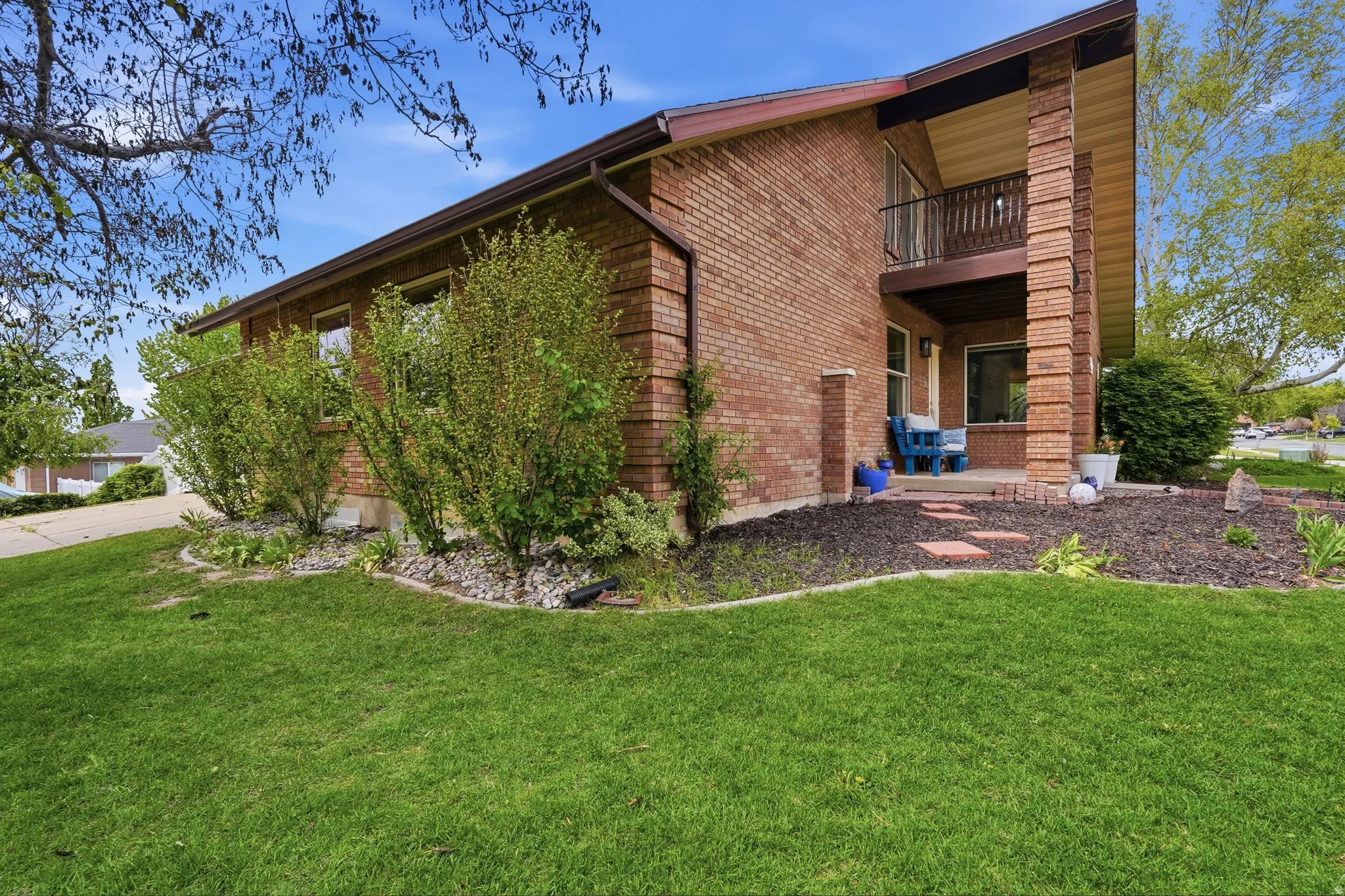 View of side of property featuring a lawn, a patio, brick siding, and a balcony