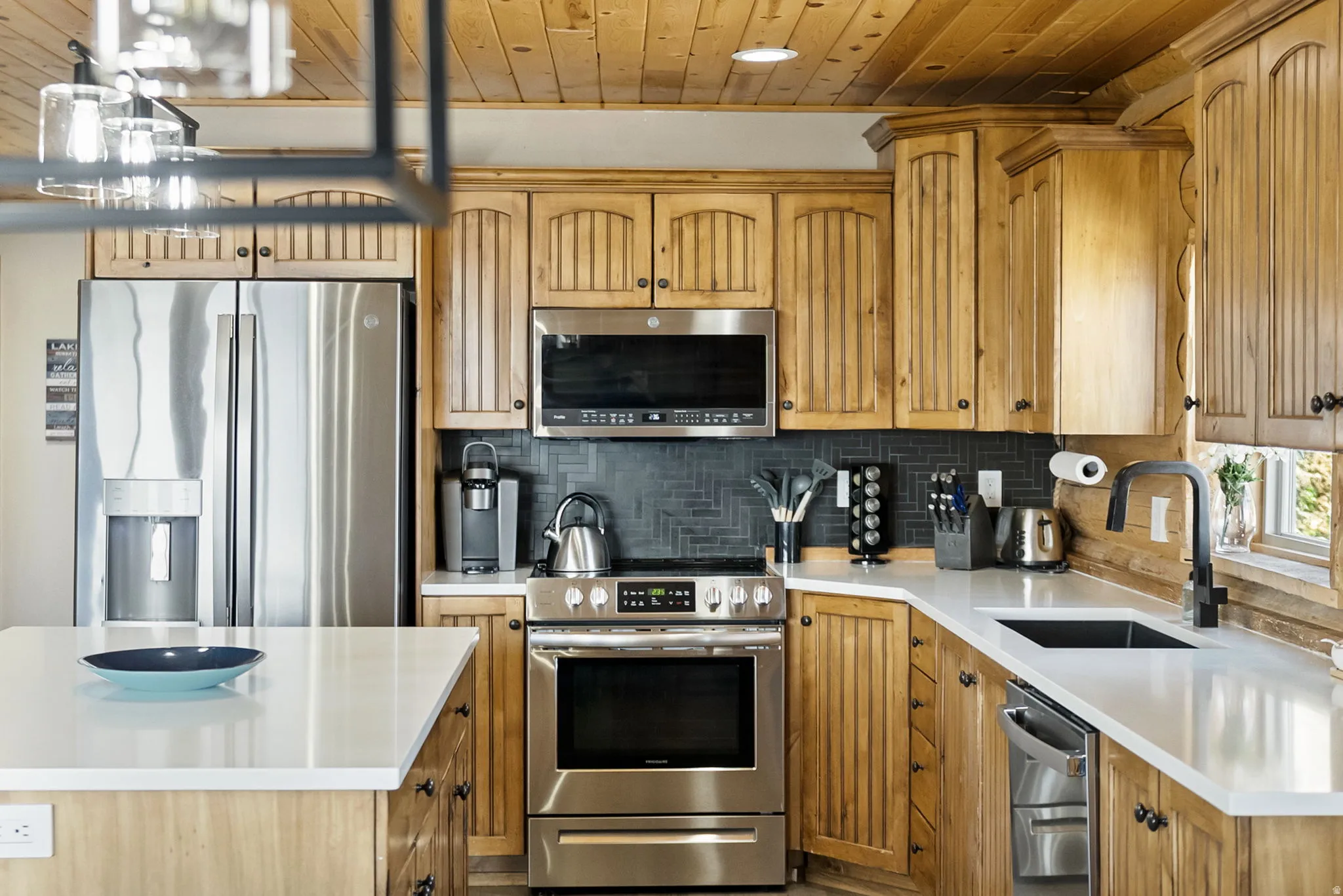 Kitchen featuring stainless steel appliances, decorative backsplash, light stone counters, wood finish cabinets, and wood ceiling
