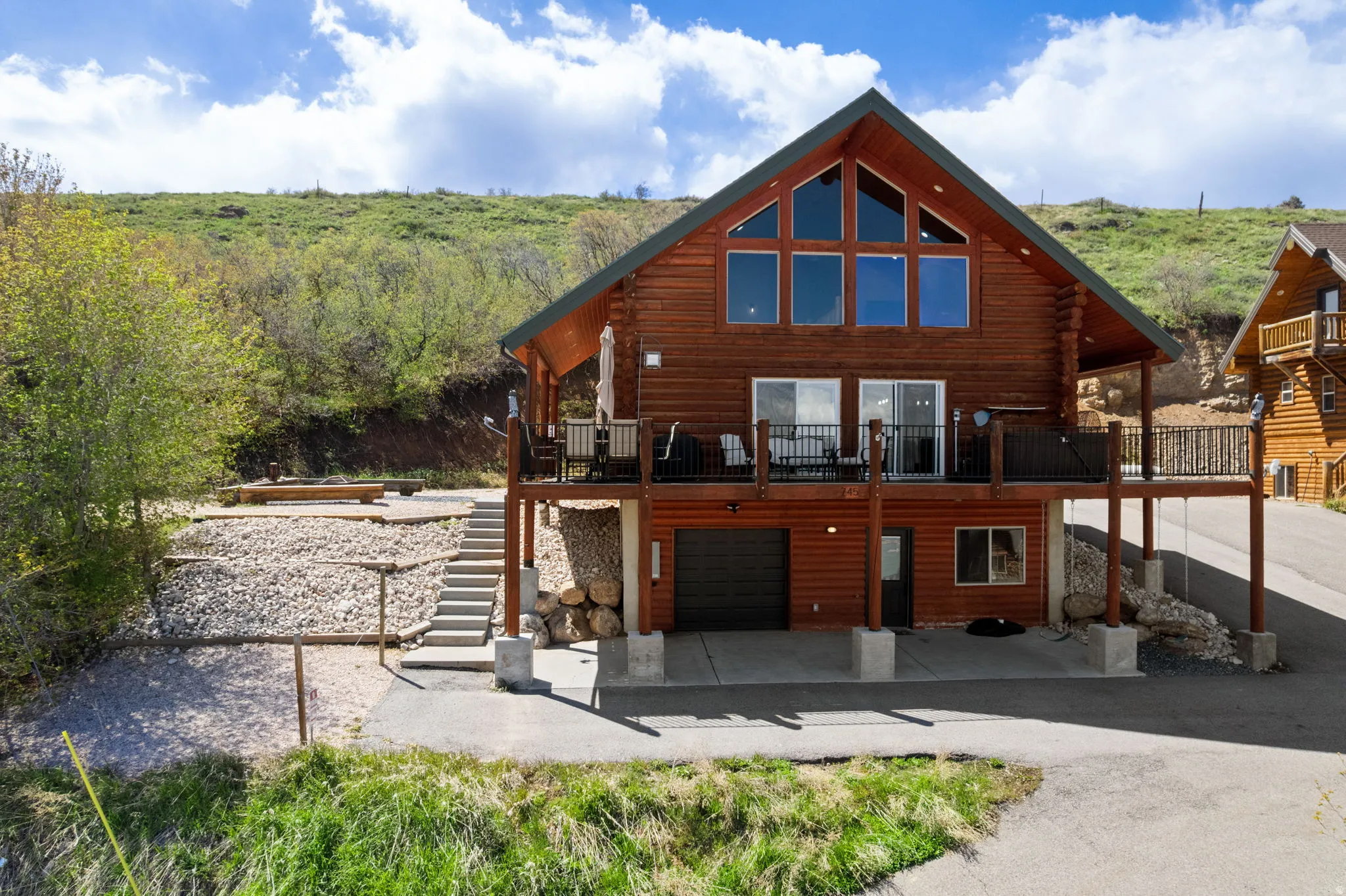 Rear view of house featuring a wooden deck, an attached garage, a patio area, log exterior, and driveway