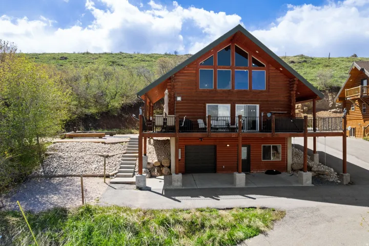 Rear view of house featuring a wooden deck, an attached garage, a patio area, log exterior, and driveway