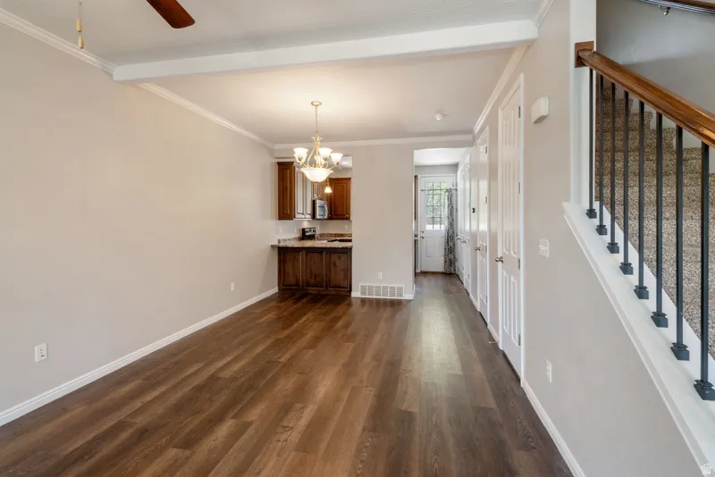 Unfurnished dining area with ornamental molding, hanging lights, a ceiling fan, dark wood-style flooring, and beam ceiling