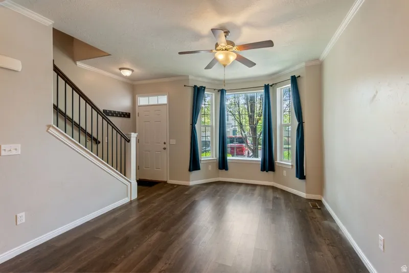 Entrance foyer featuring ornamental molding, dark wood finished floors, ceiling fan, and a textured ceiling