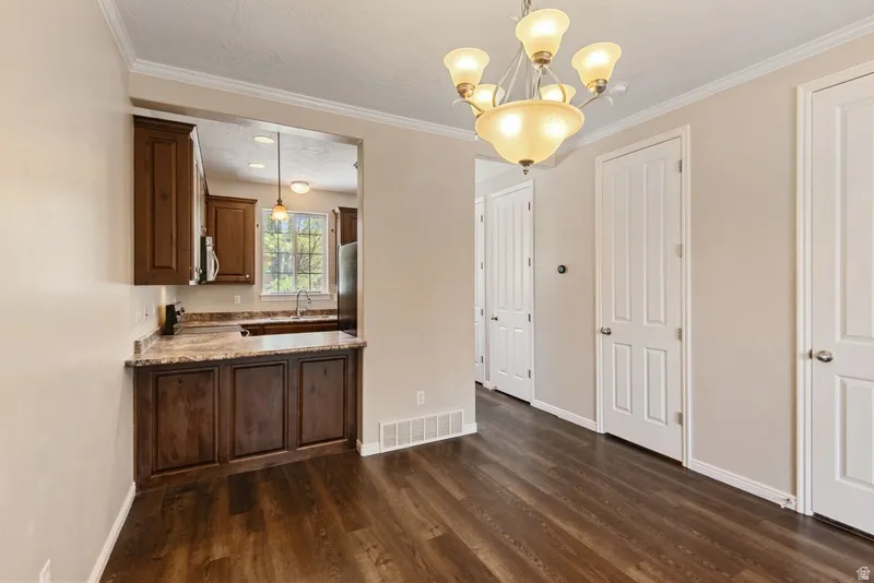 Unfurnished dining area featuring dark wood-type flooring, hanging lights, a textured ceiling, and crown molding