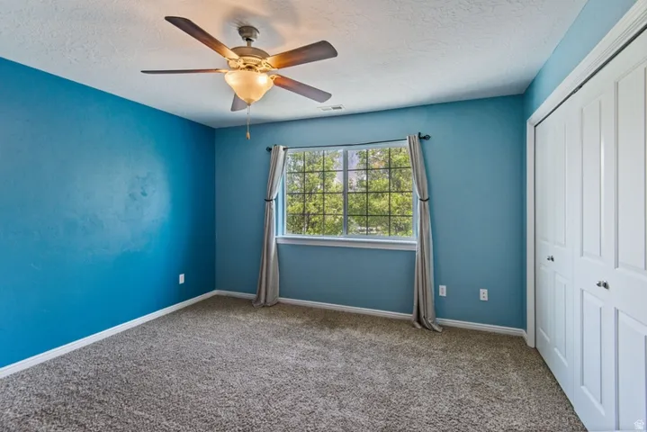 Unfurnished bedroom featuring a closet, carpet flooring, a textured ceiling, and a ceiling fan