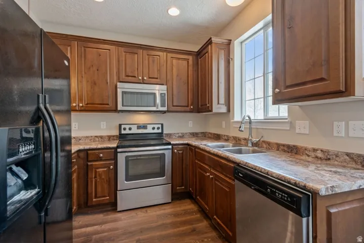Kitchen with stainless steel appliances, dark wood-style floors, wood finish cabinets, a textured ceiling, and recessed lighting