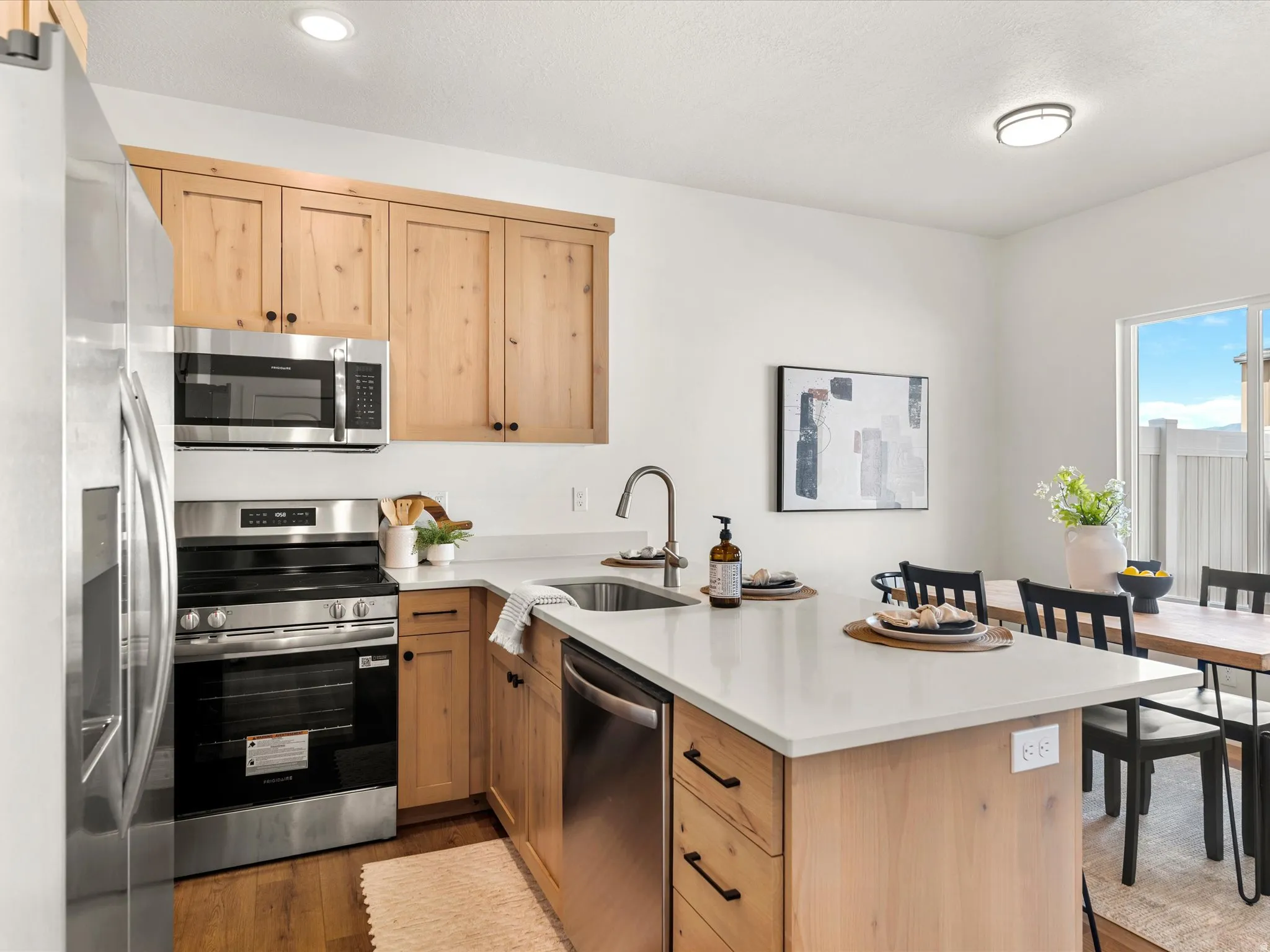 Kitchen featuring a peninsula, stainless steel appliances, light wood finish cabinetry, and dark wood-style flooring