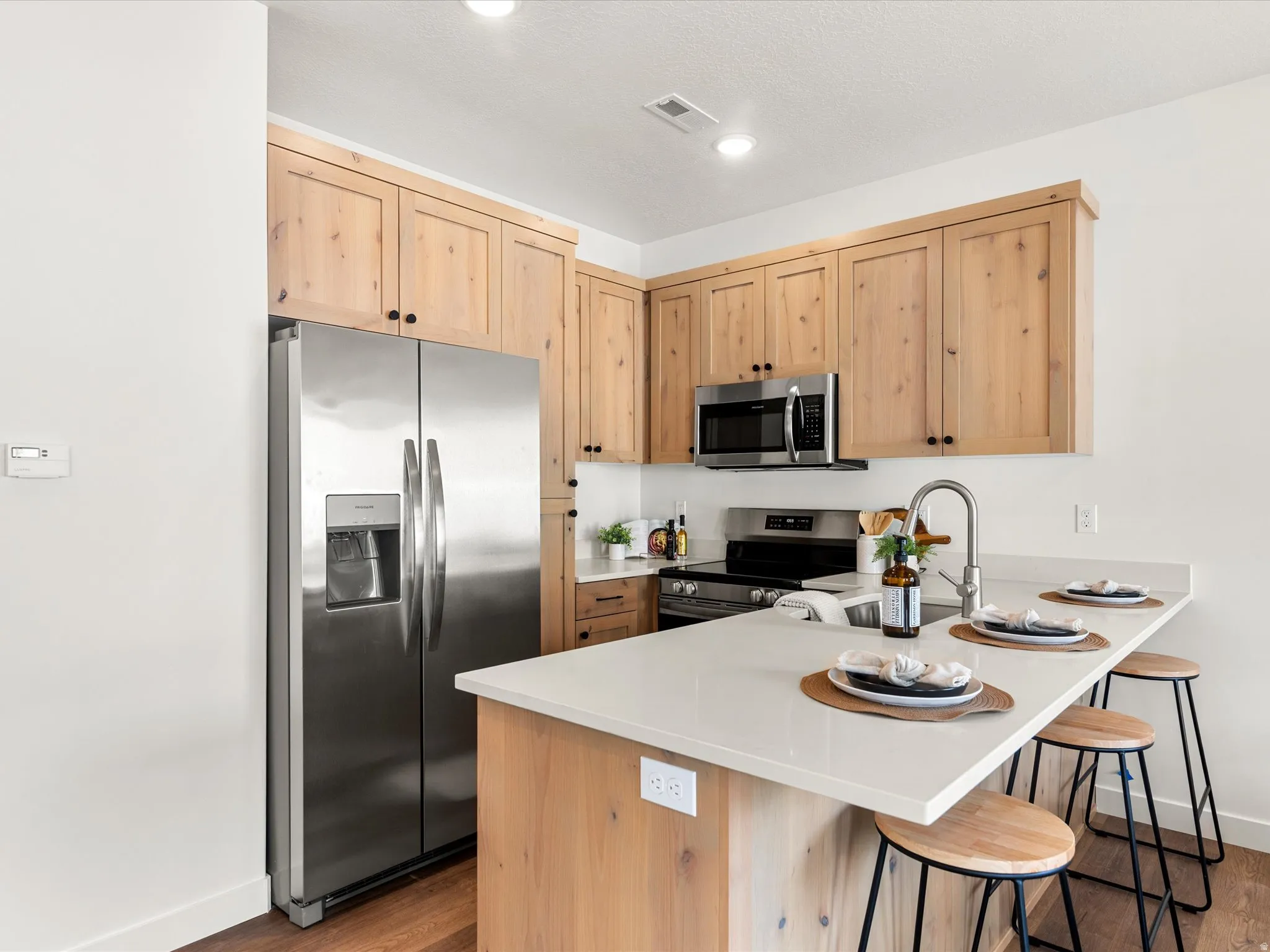 Kitchen featuring light wood finish cabinets, stainless steel appliances, a peninsula, a breakfast bar area, and recessed lighting