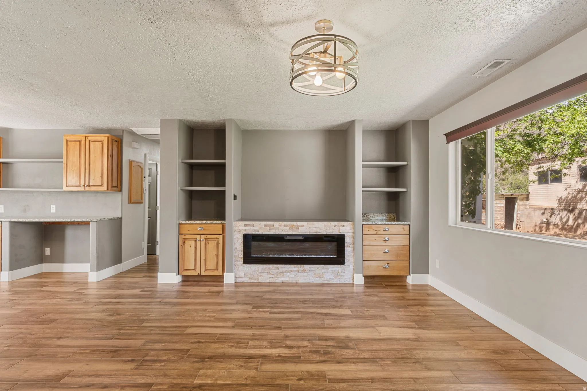 Unfurnished living room featuring built in features, a textured ceiling, a stone fireplace, and light wood-style flooring