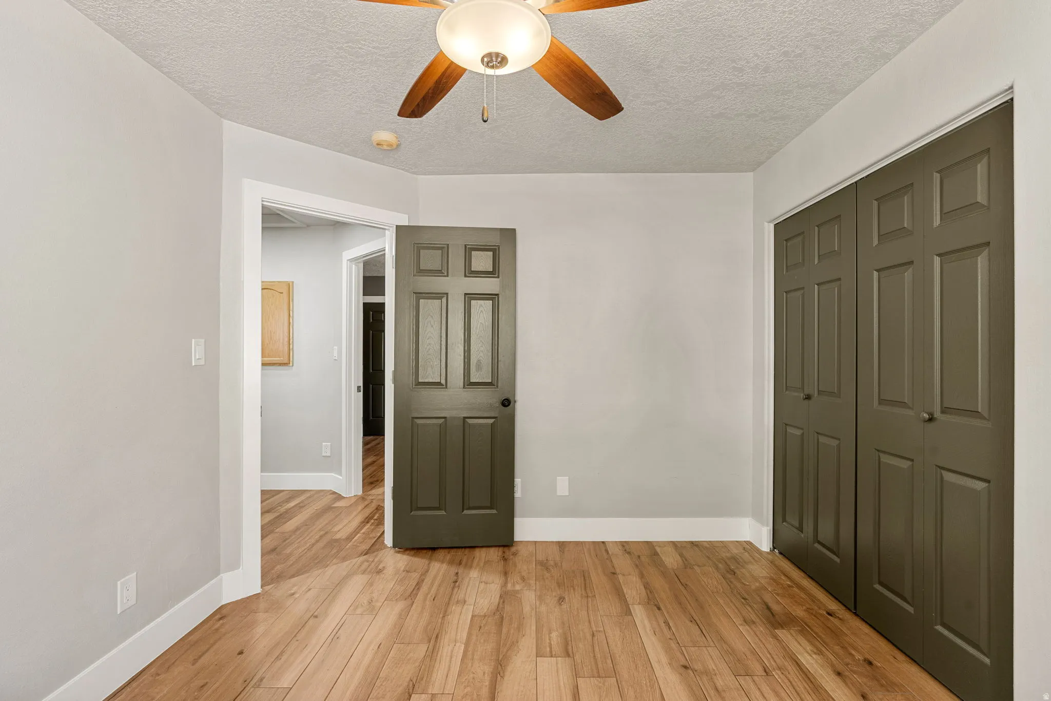 Unfurnished bedroom featuring light wood finished floors, a closet, ceiling fan, and a textured ceiling