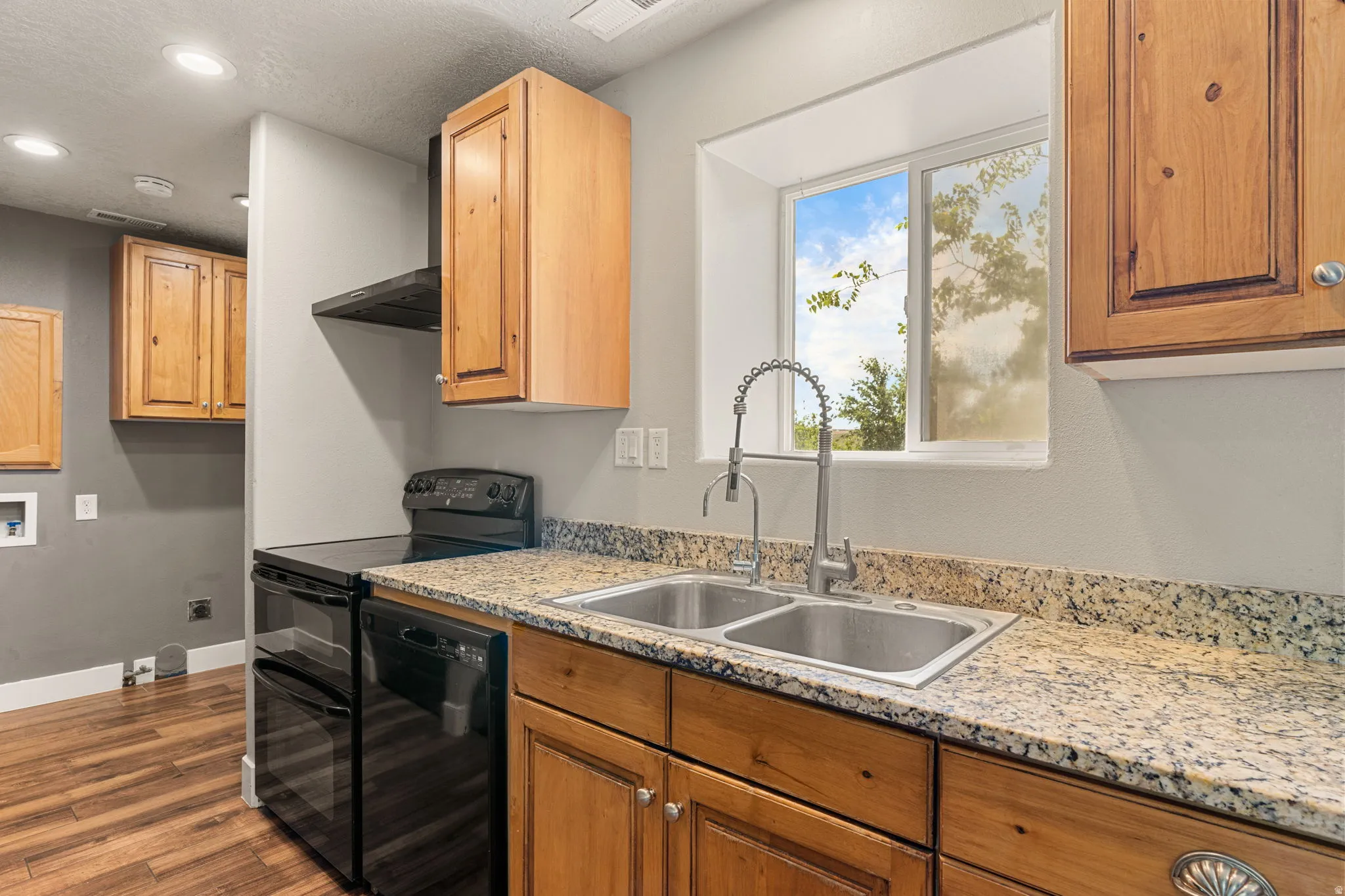 Kitchen with black appliances, light stone countertops, dark wood-style flooring, recessed lighting, and wood finish cabinetry