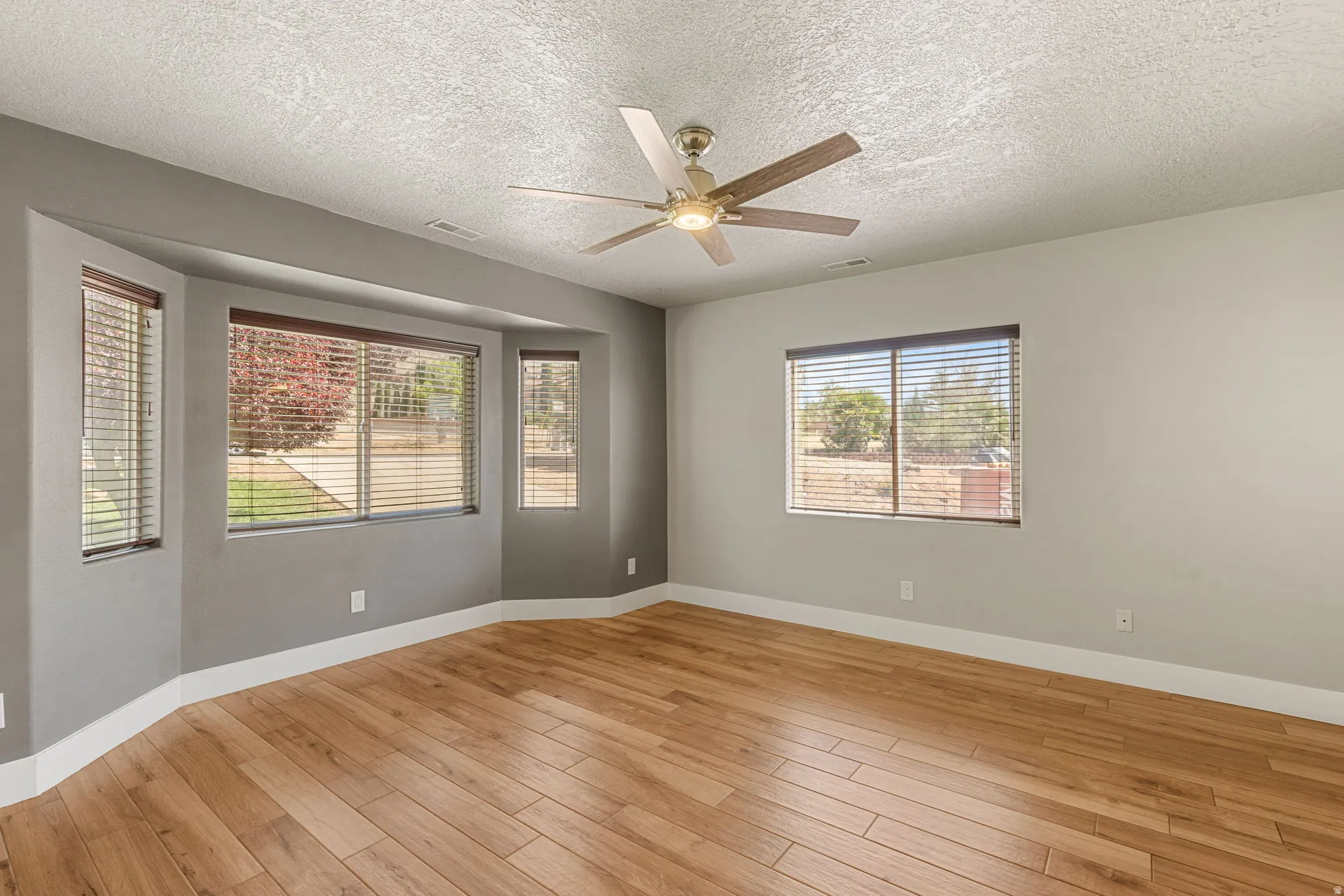 Primary  with light wood-style floors, ceiling fan, and a textured ceiling