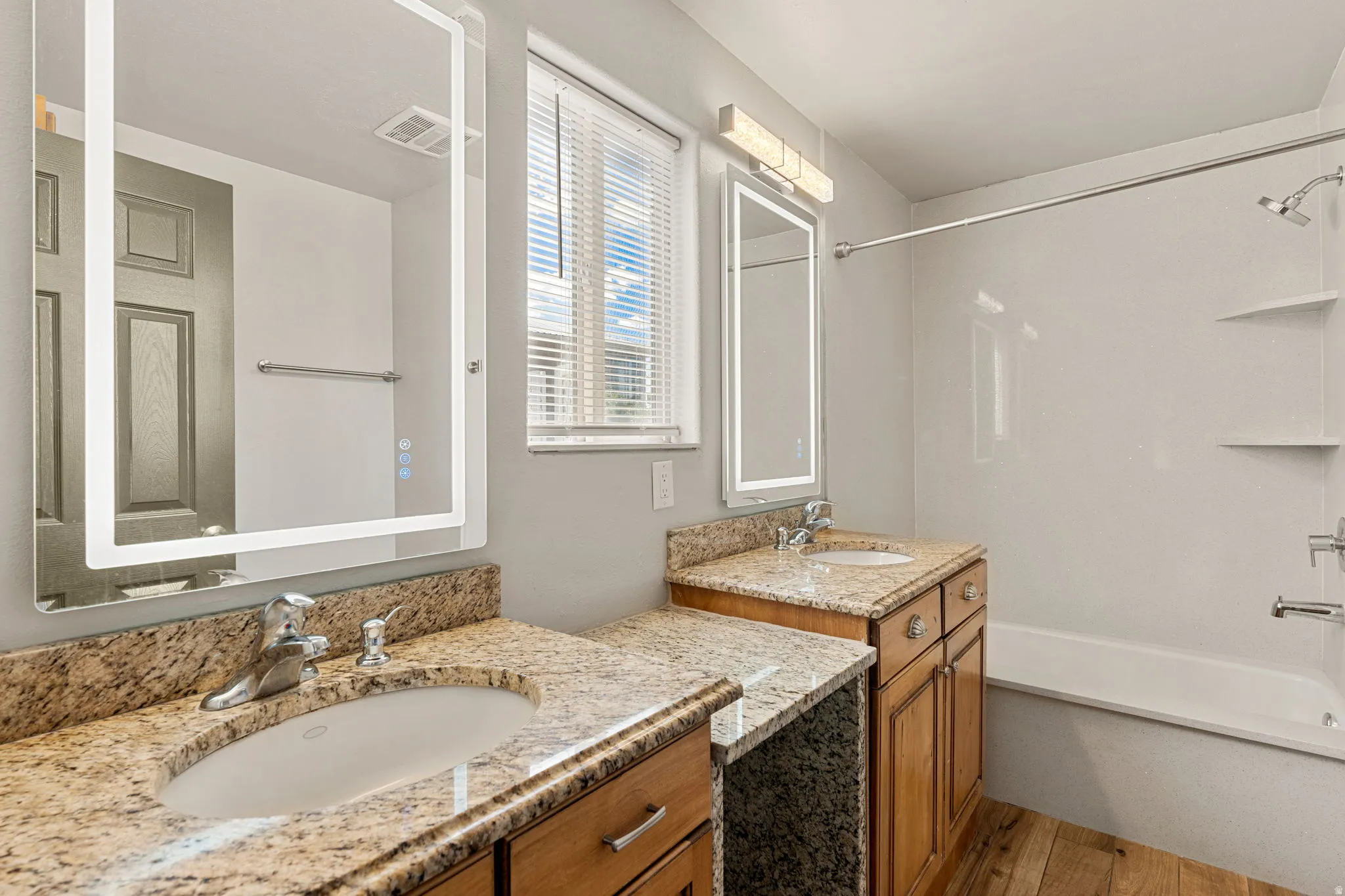 Primary Bathroom featuring two vanities, bathtub / shower combination, and light wood-type flooring