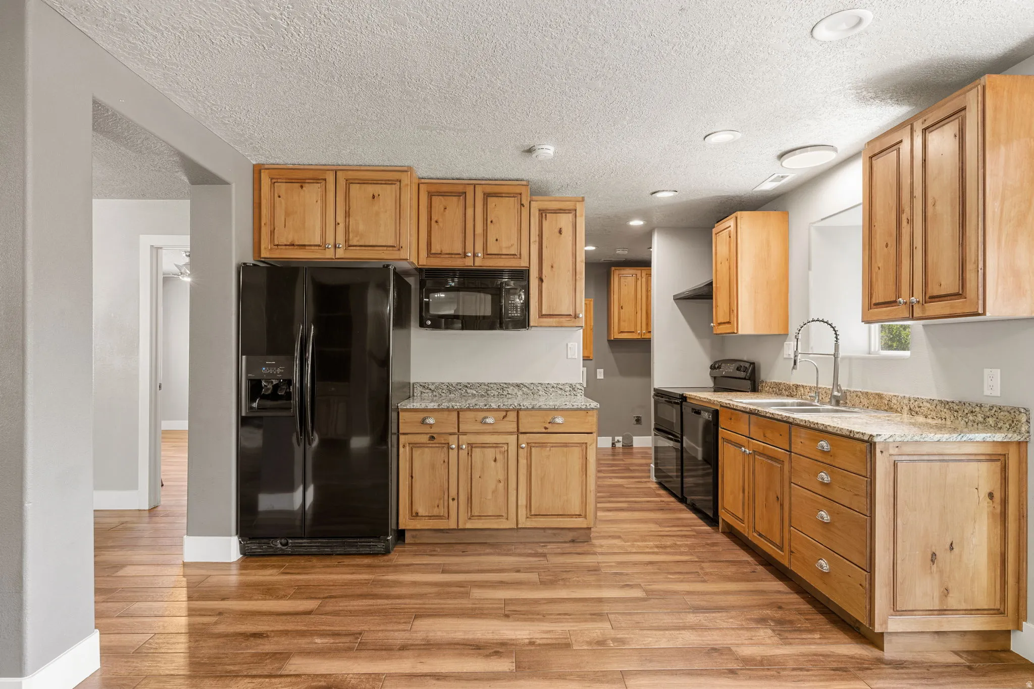 Kitchen featuring black appliances, light stone counters, light wood-style floors, recessed lighting, and a textured ceiling