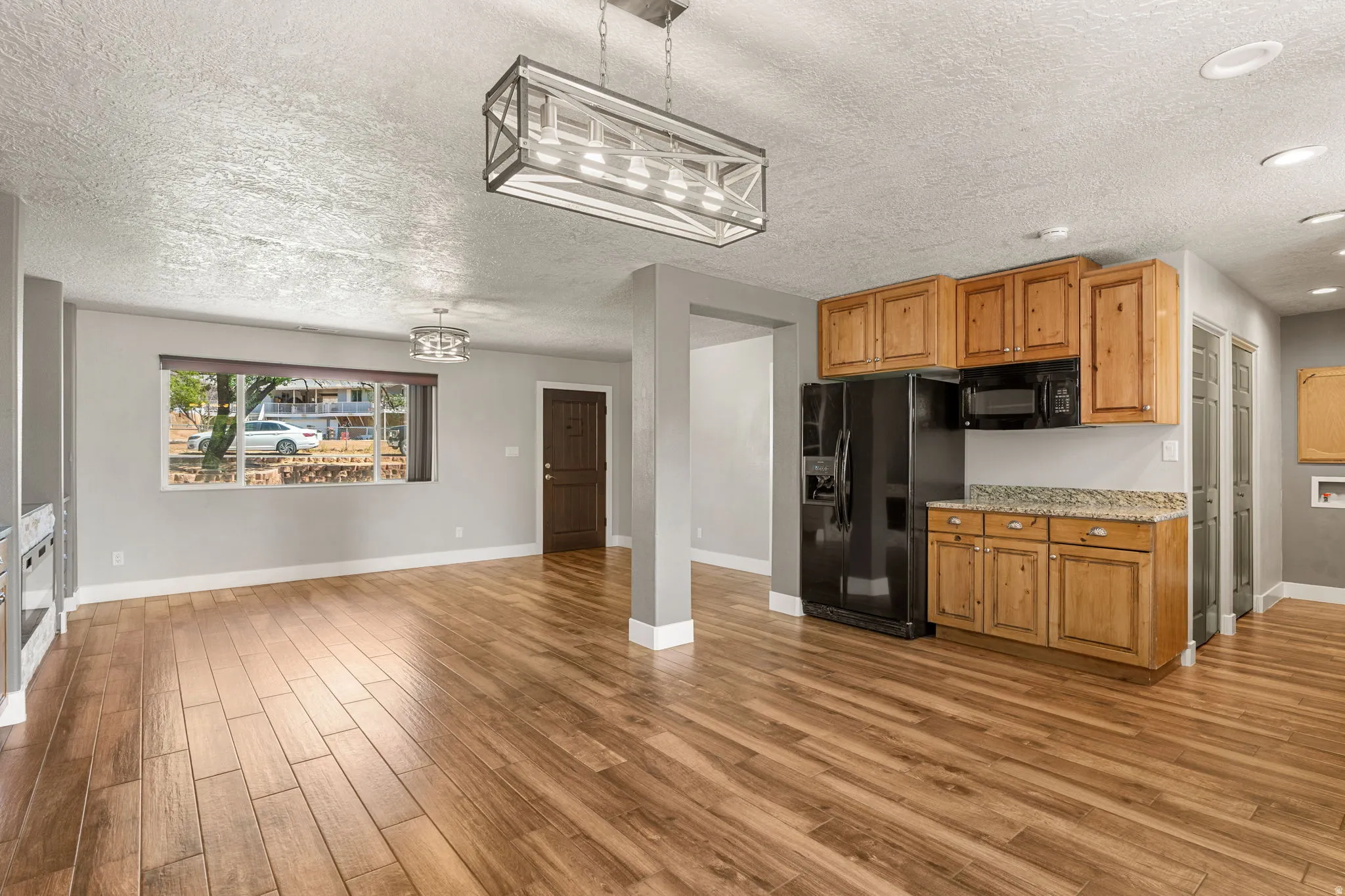 Kitchen featuring black appliances, a textured ceiling, light wood-style flooring, decorative light fixtures, and light stone counters