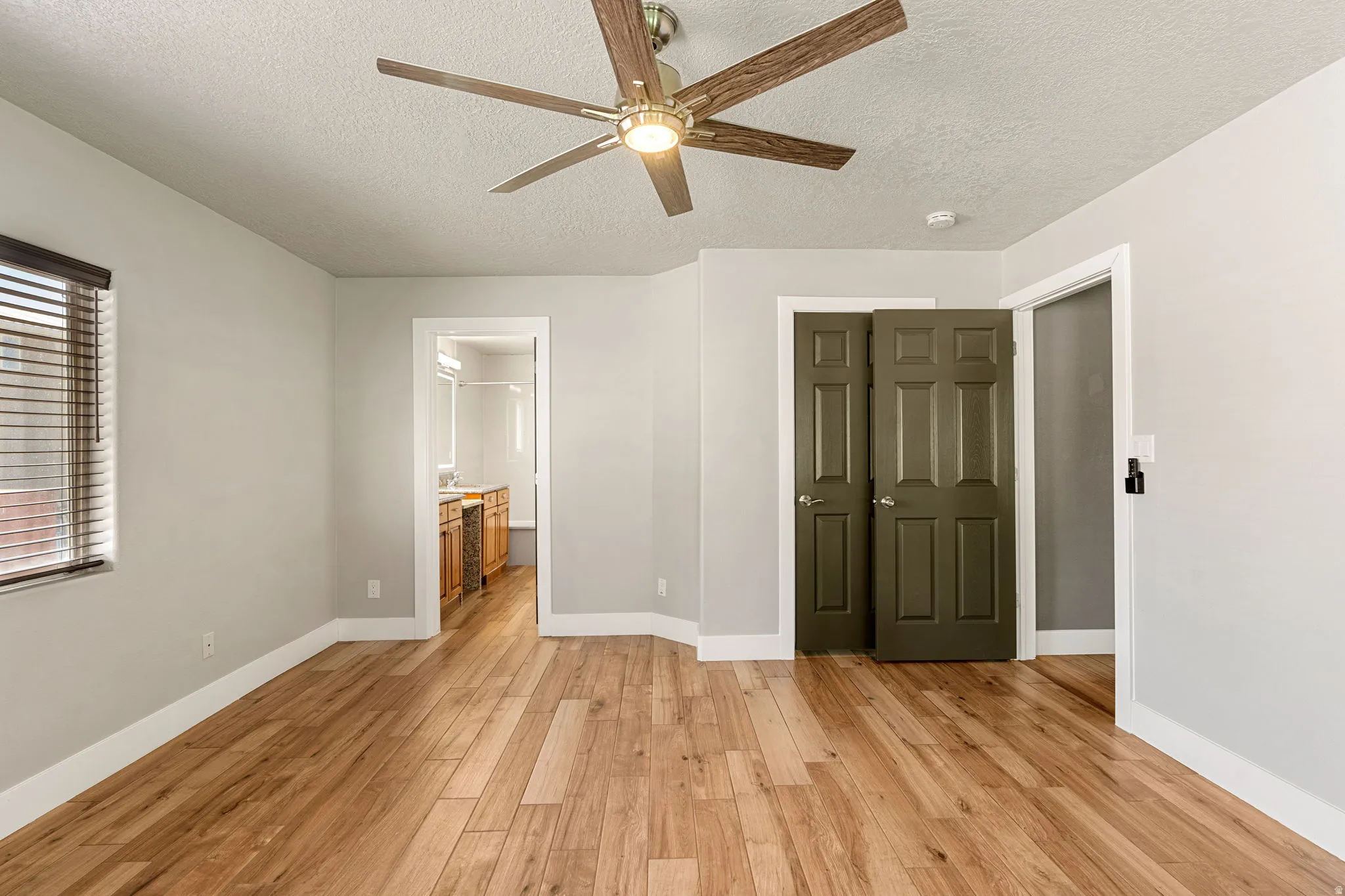 Unfurnished bedroom featuring light wood-type flooring, a textured ceiling, a ceiling fan, and connected bathroom