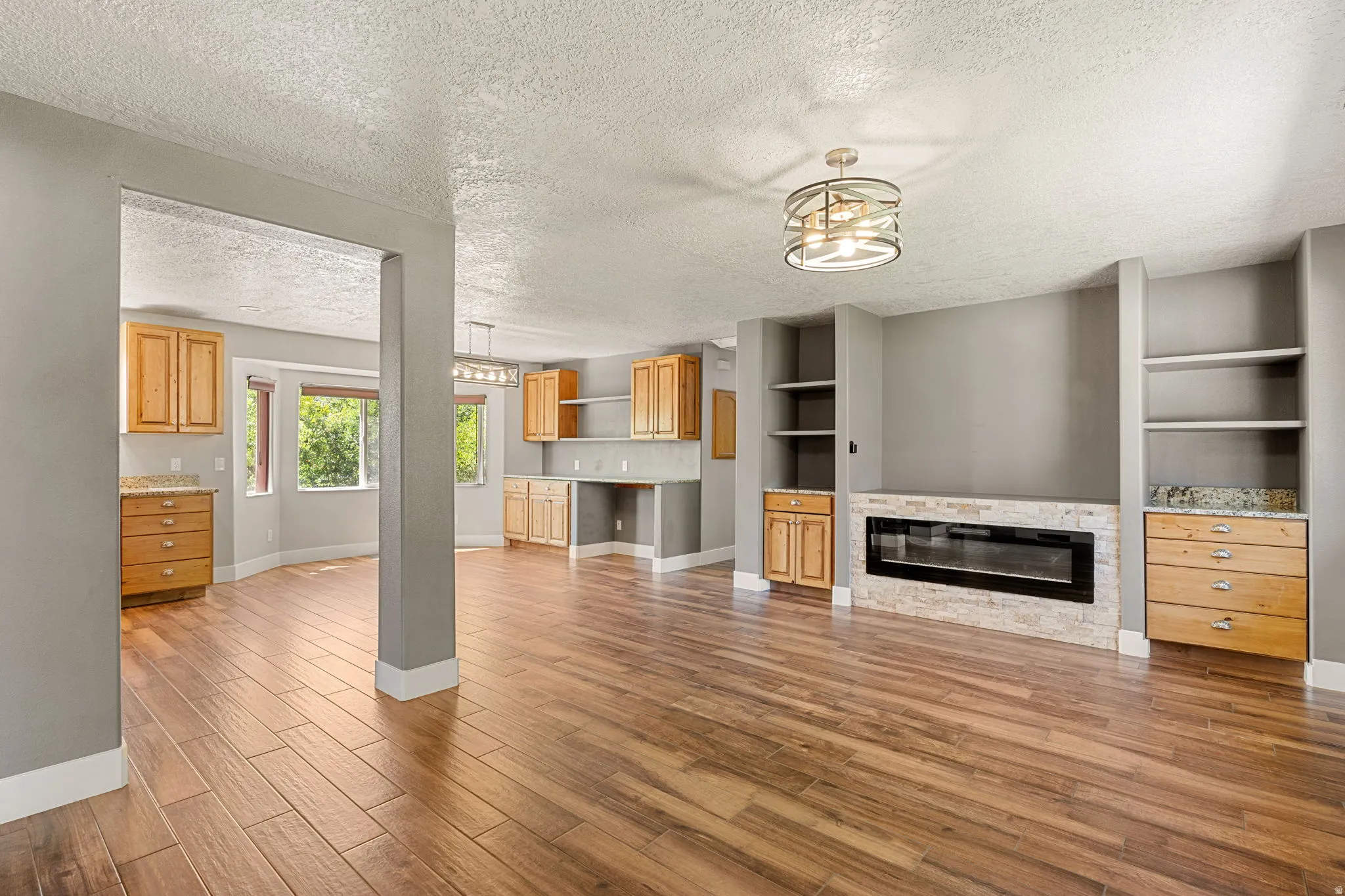 Unfurnished living room featuring a textured ceiling, light wood finished floors, a stone fireplace, and built in features