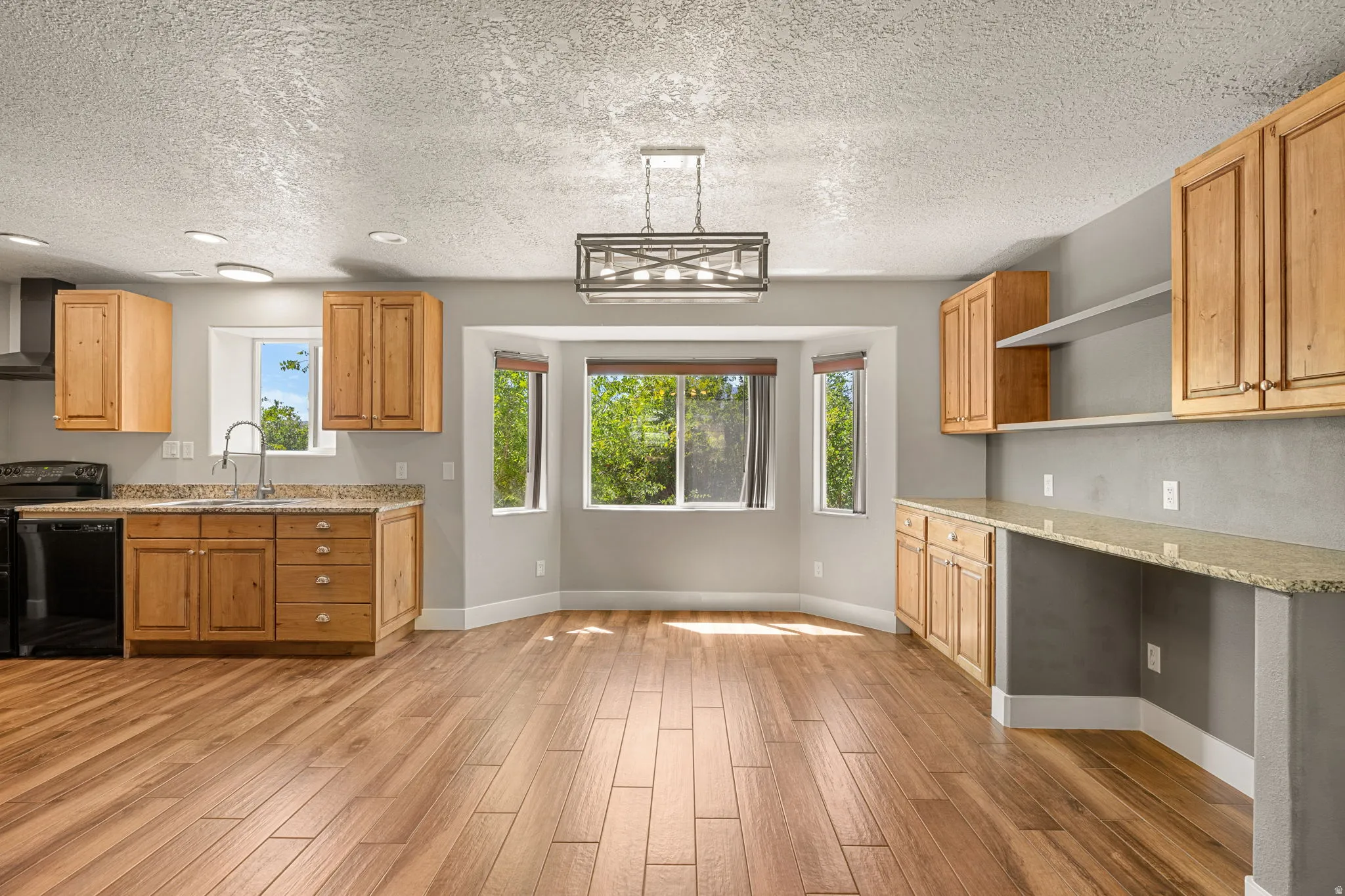 Kitchen with light stone countertops, black appliances, open shelves, light wood-type flooring, and a textured ceiling