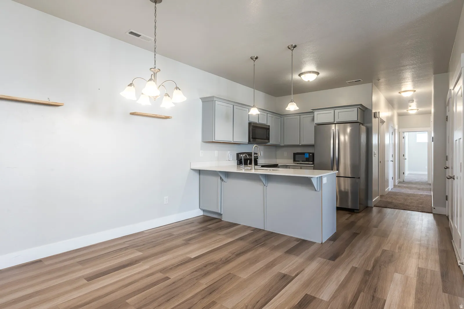 Kitchen with gray cabinetry, stainless steel appliances, a peninsula, a breakfast bar, and hanging lights