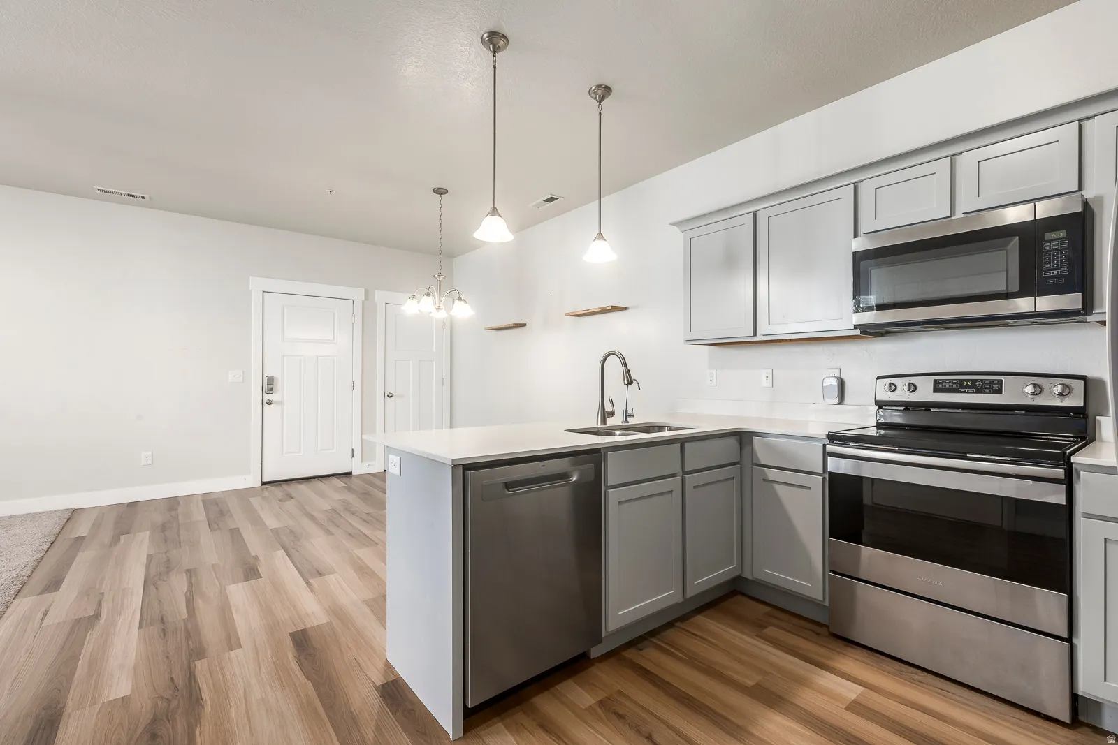 Kitchen featuring stainless steel appliances, gray cabinetry, light wood-style flooring, a peninsula, and a chandelier