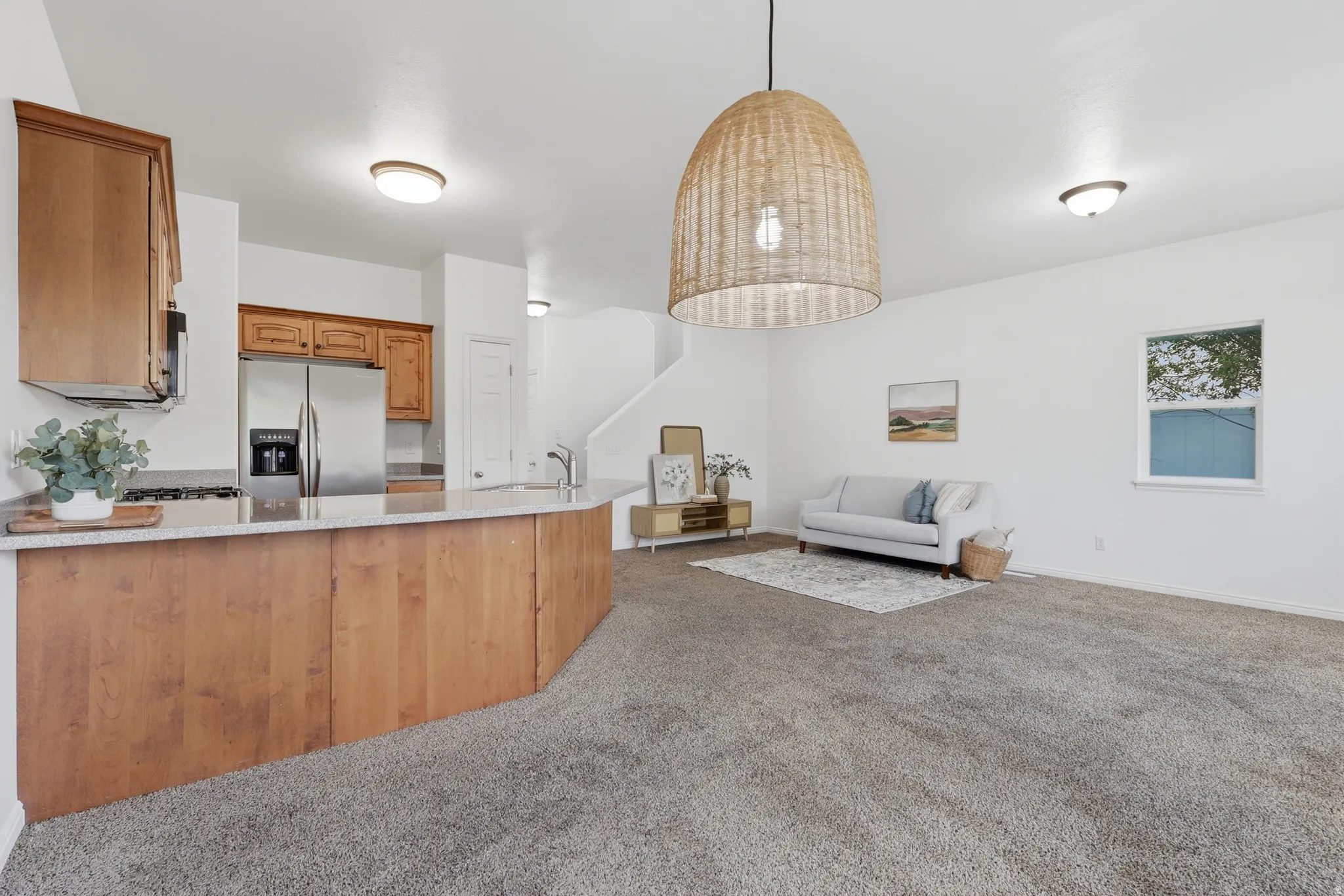 Kitchen with wood finish cabinetry, open floor plan, stainless steel refrigerator with ice dispenser, light colored carpet, and light stone countertops