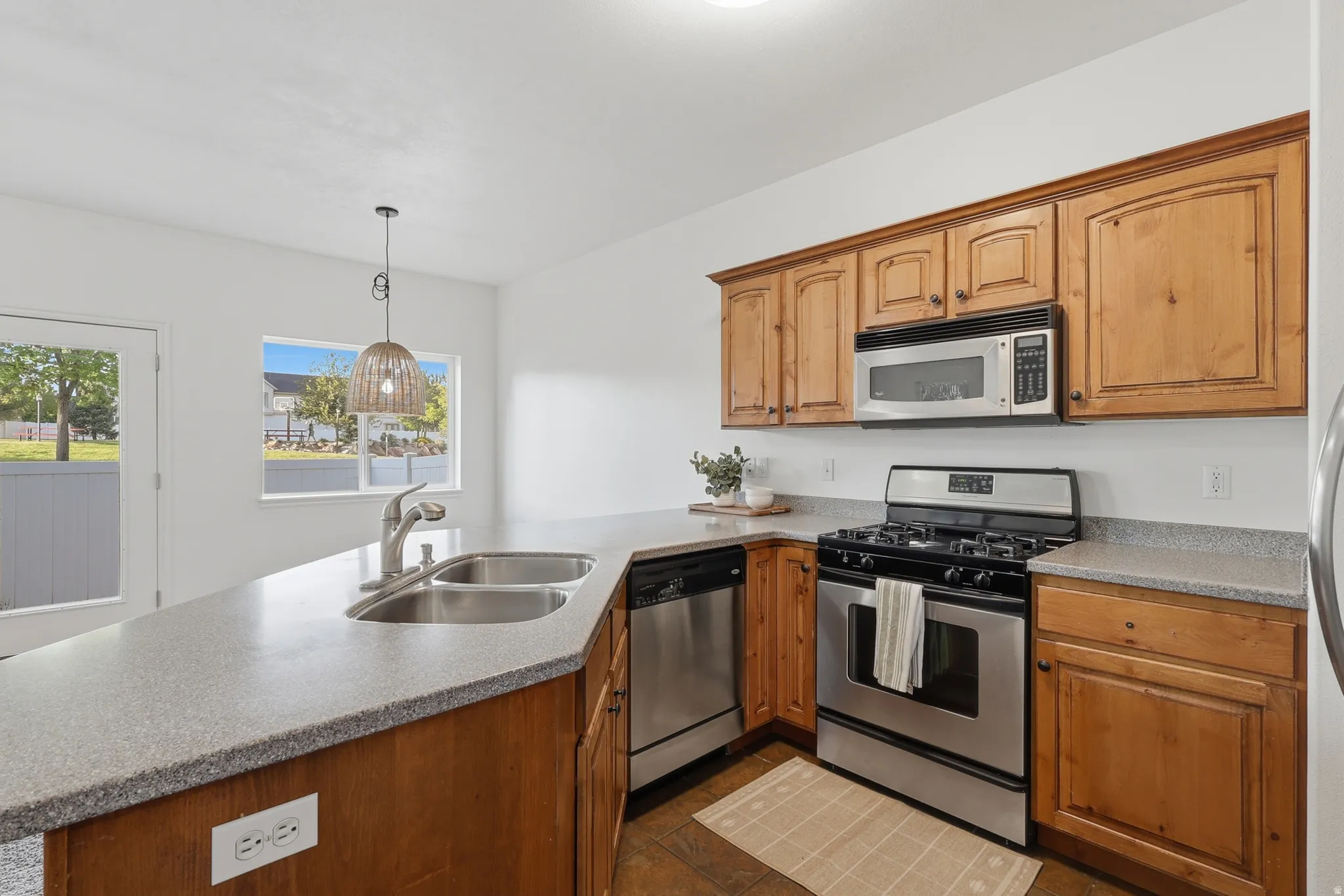 Kitchen with stainless steel appliances, a peninsula, decorative light fixtures, and wood finish cabinetry