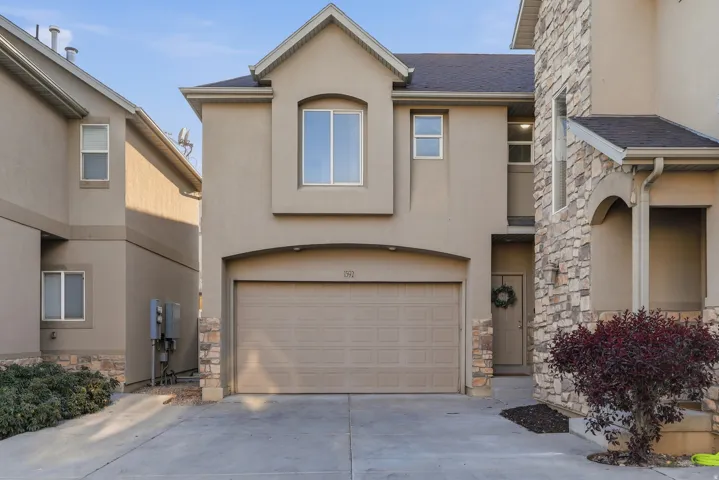 View of front facade featuring stone siding, stucco siding, a garage, and driveway