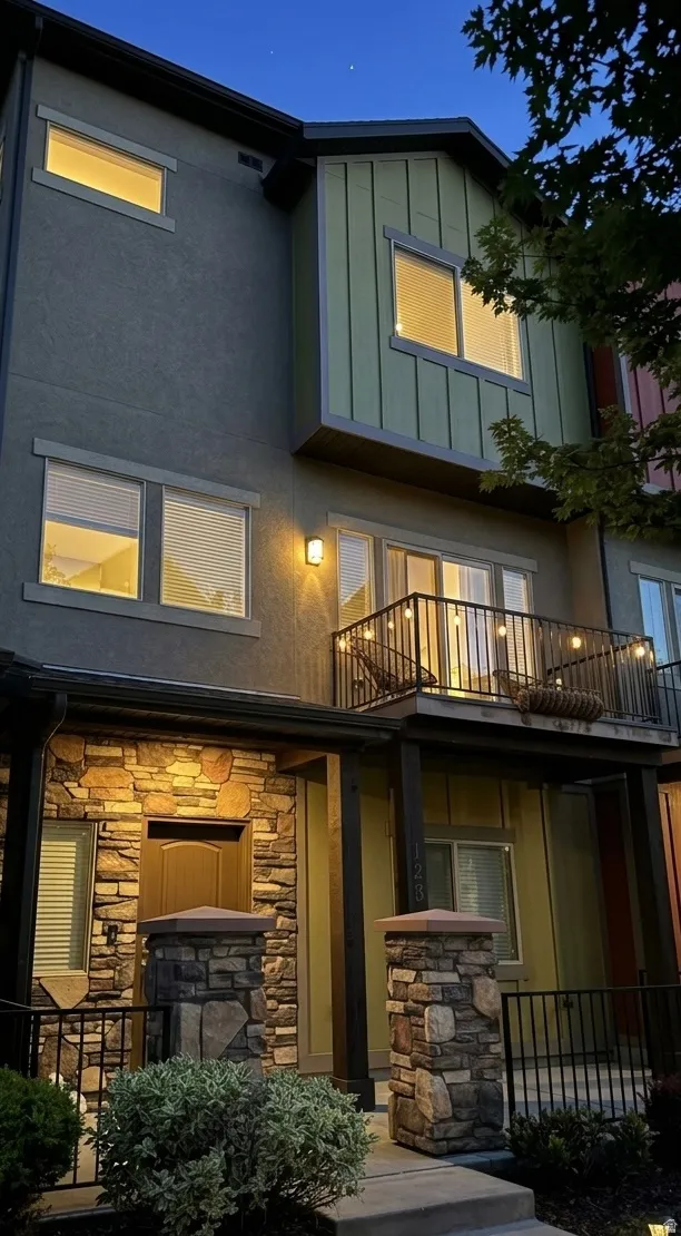 Back of house featuring a balcony, stone siding, and stucco siding