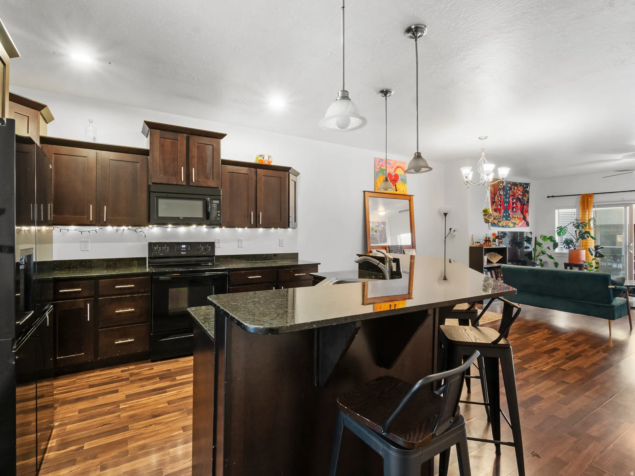 Kitchen featuring black appliances, dark wood finish cabinets, a kitchen island with sink, and open floor plan
