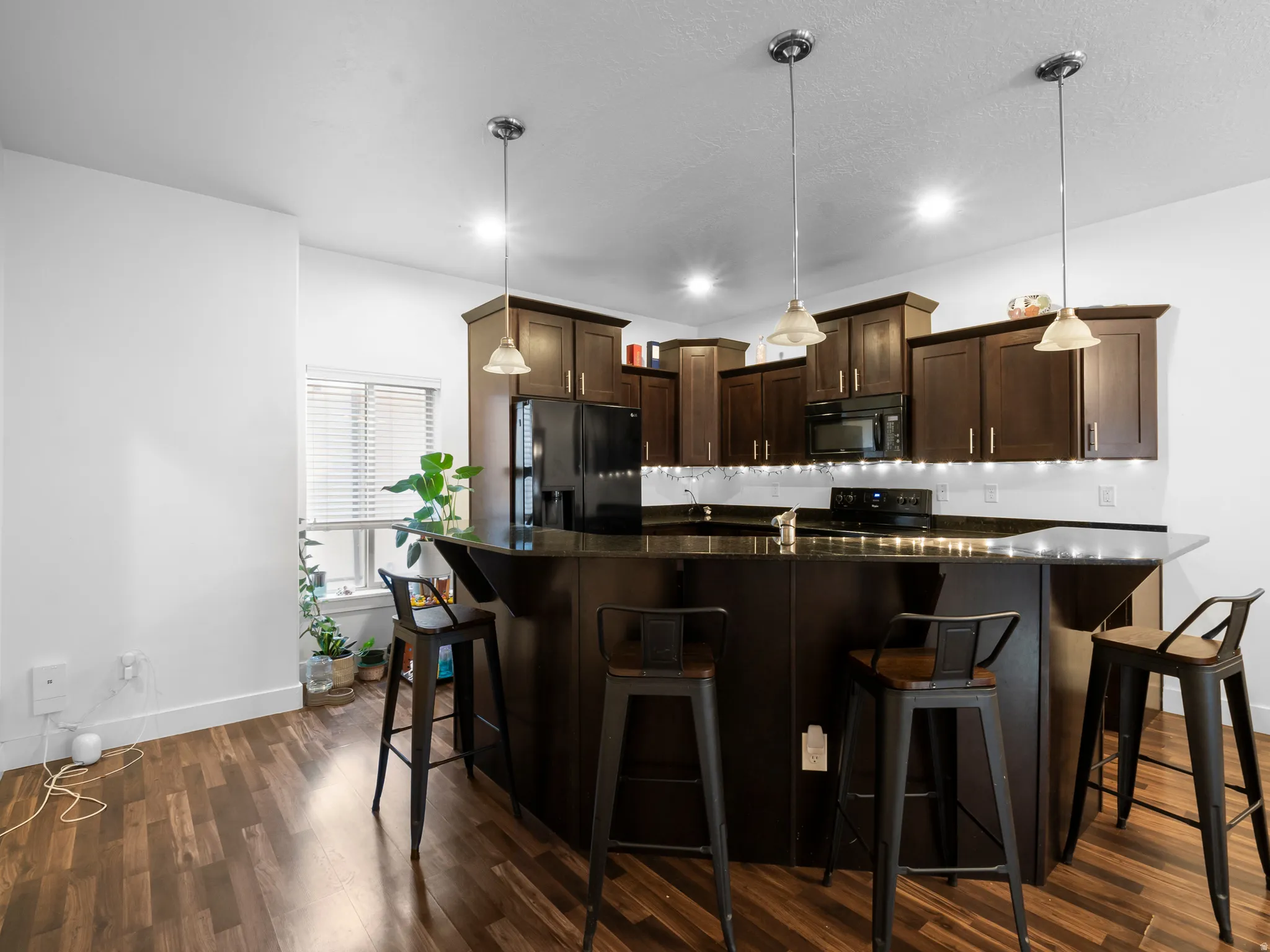 Kitchen featuring dark wood finish cabinetry, black appliances, a breakfast bar area, and dark stone countertops